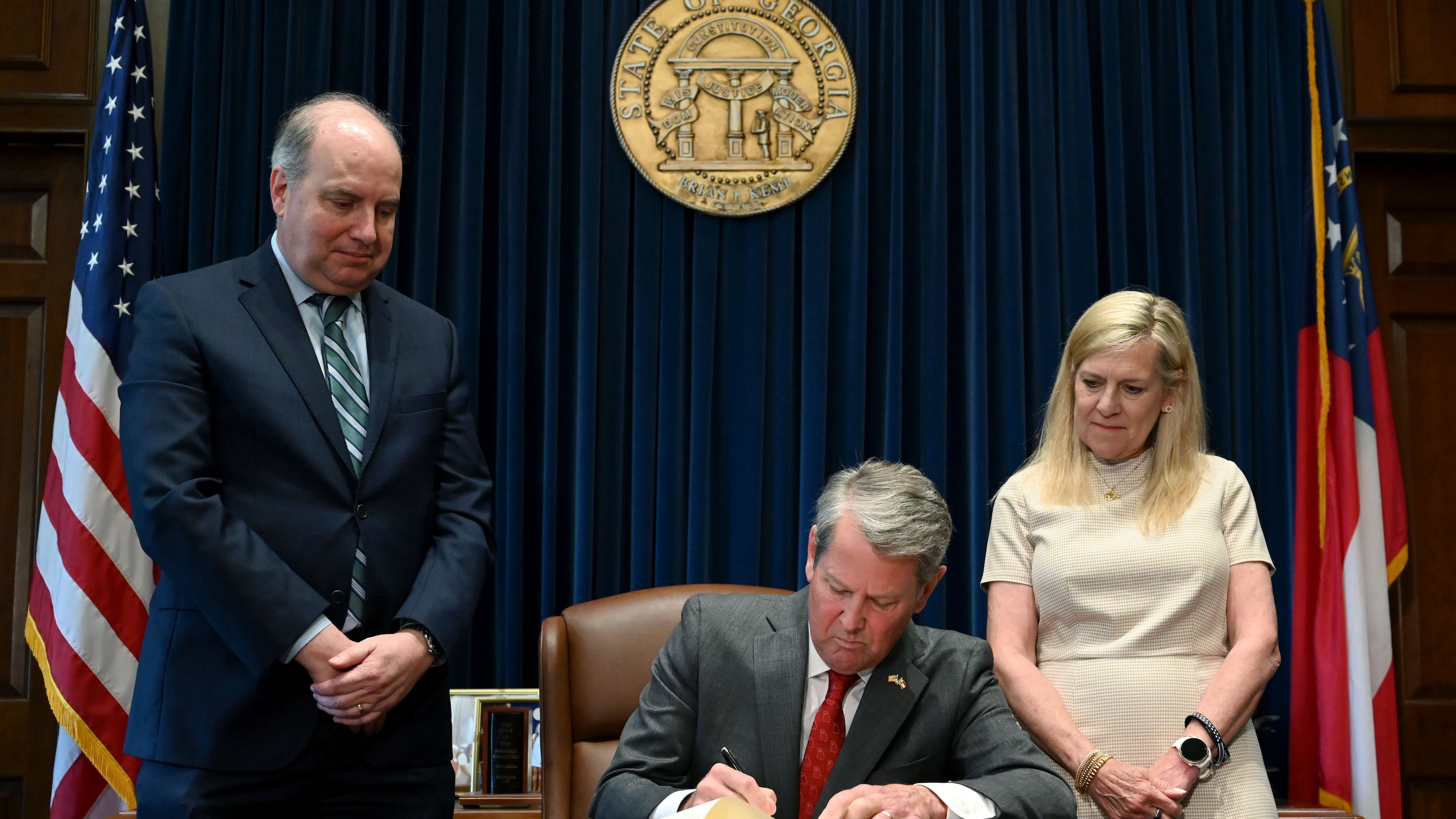 Gov. Brian Kemp (center) signs the state's new budget alongside Rick Dunn (left), director of the Governor's Office of Planning and Budget, and first lady Marty Kemp. (Hyosub Shin/AJC)