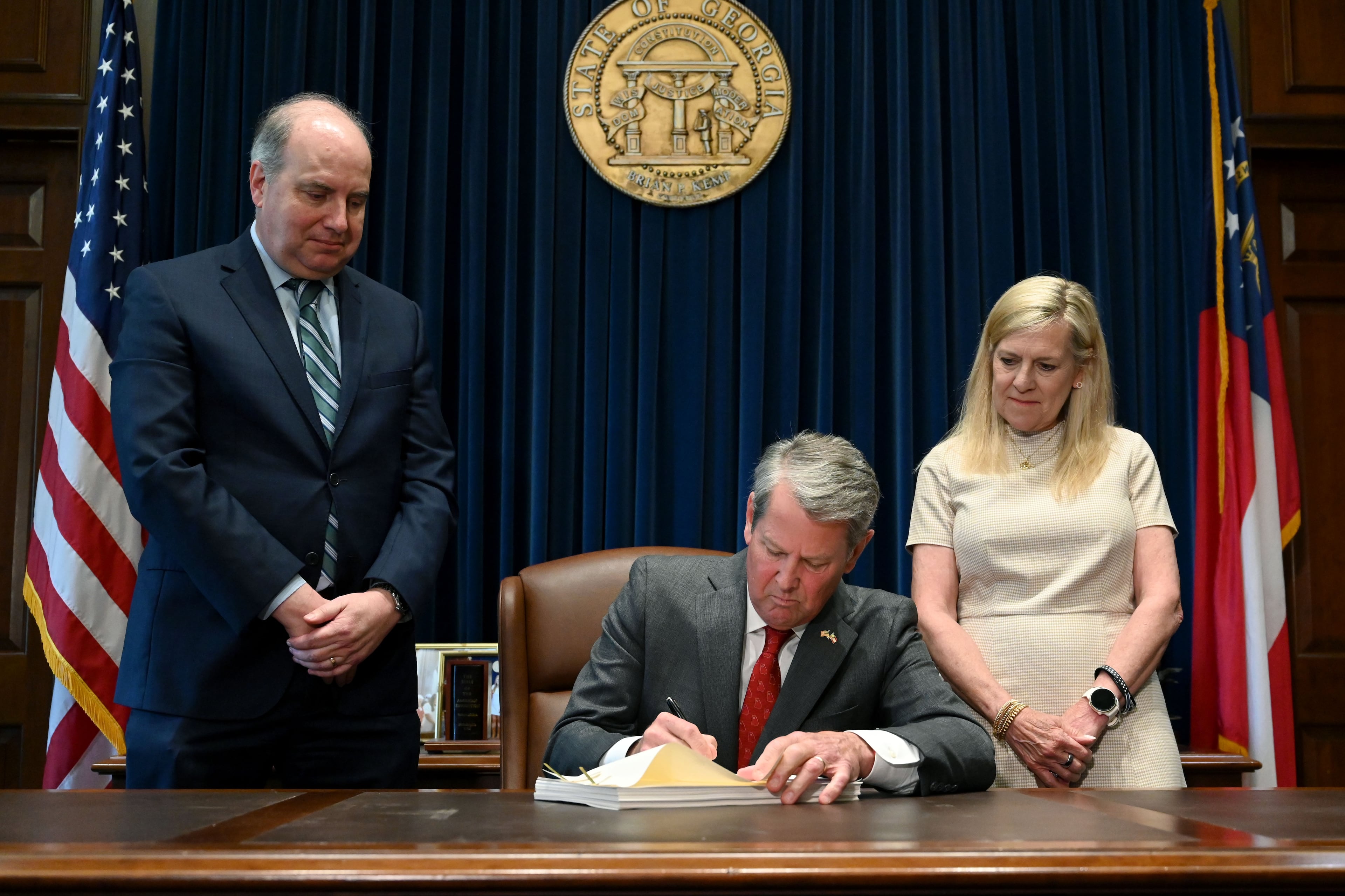 Gov. Brian Kemp (center) signs the state’s new budget alongside Rick Dunn (left), director of the Governor’s Office of Planning and Budget, and first lady Marty Kemp. (Hyosub Shin/AJC)
