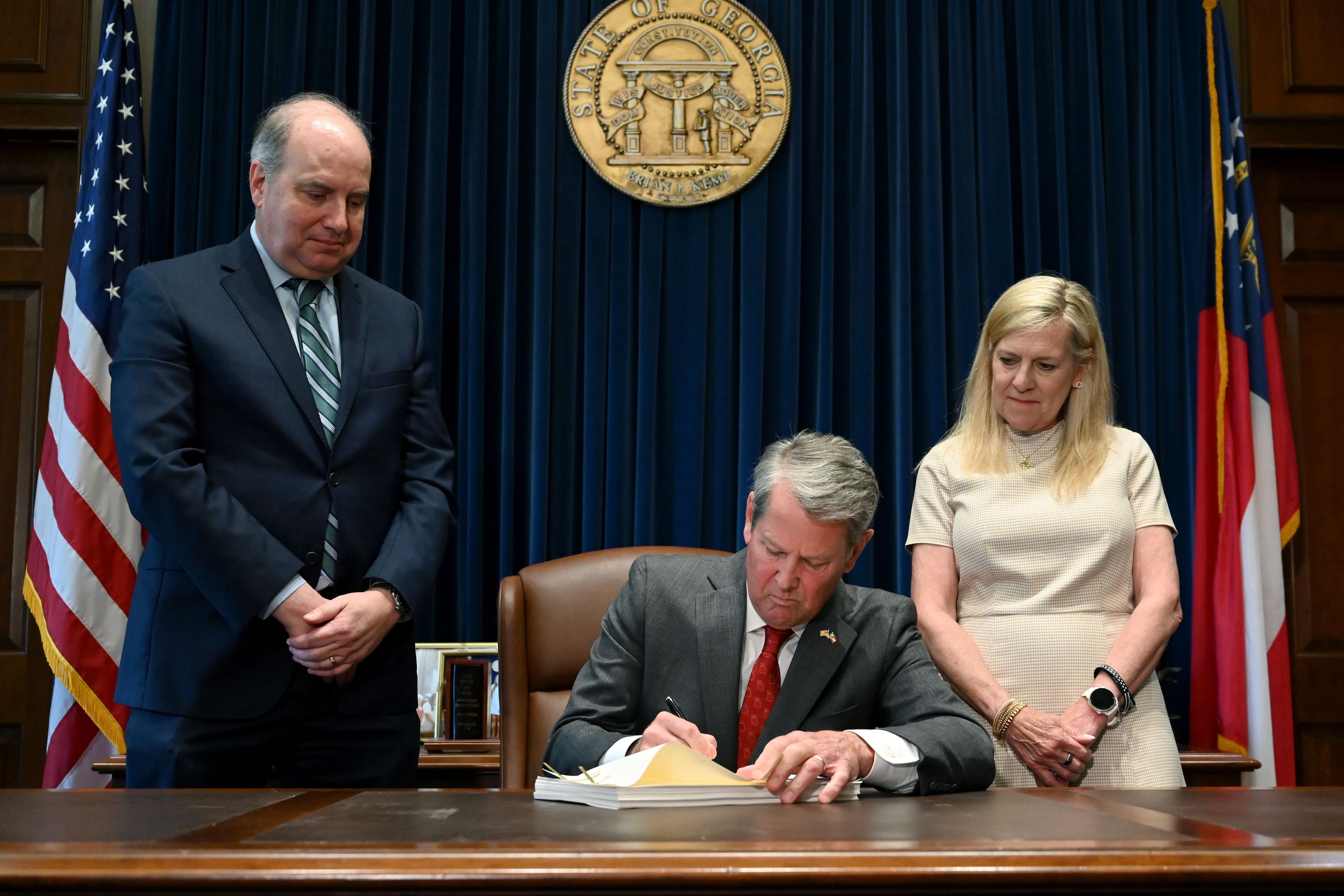 Gov. Brian Kemp (center) signs the state's new budget alongside Rick Dunn (left), director of the Governor's Office of Planning and Budget, and first lady Marty Kemp. (Hyosub Shin/AJC)