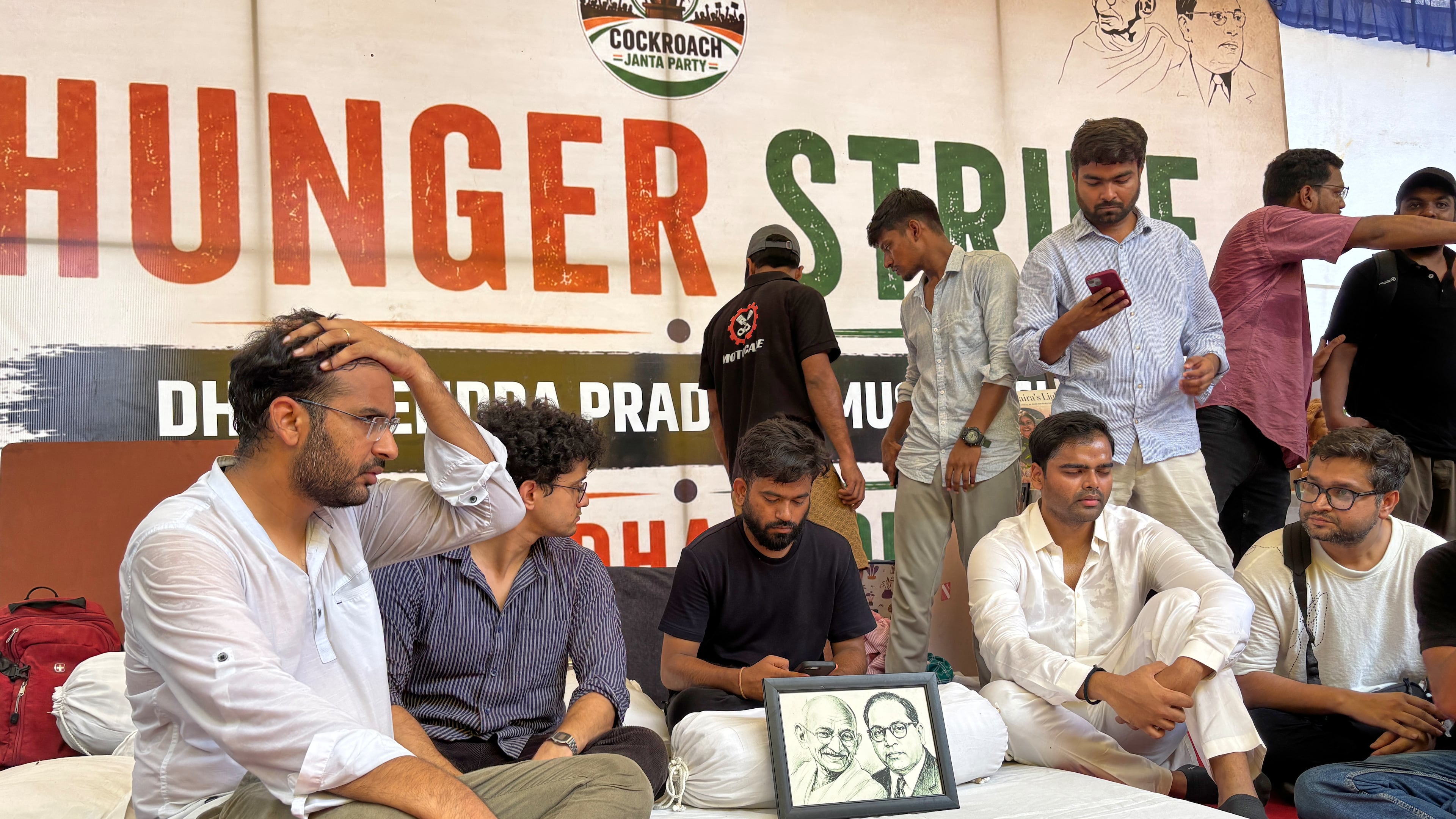 Abhijeet Dipke, founder of the Cockroach Janta Party, center sitting, starts his indefinite hunger strike during a protest demanding the resignation of Education Minister Dharmendra Pradhan over alleged examination irregularities and repeated paper leaks in New Delhi, India, Saturday, July 18, 2026. (AP Photo/Shonal Ganguly)