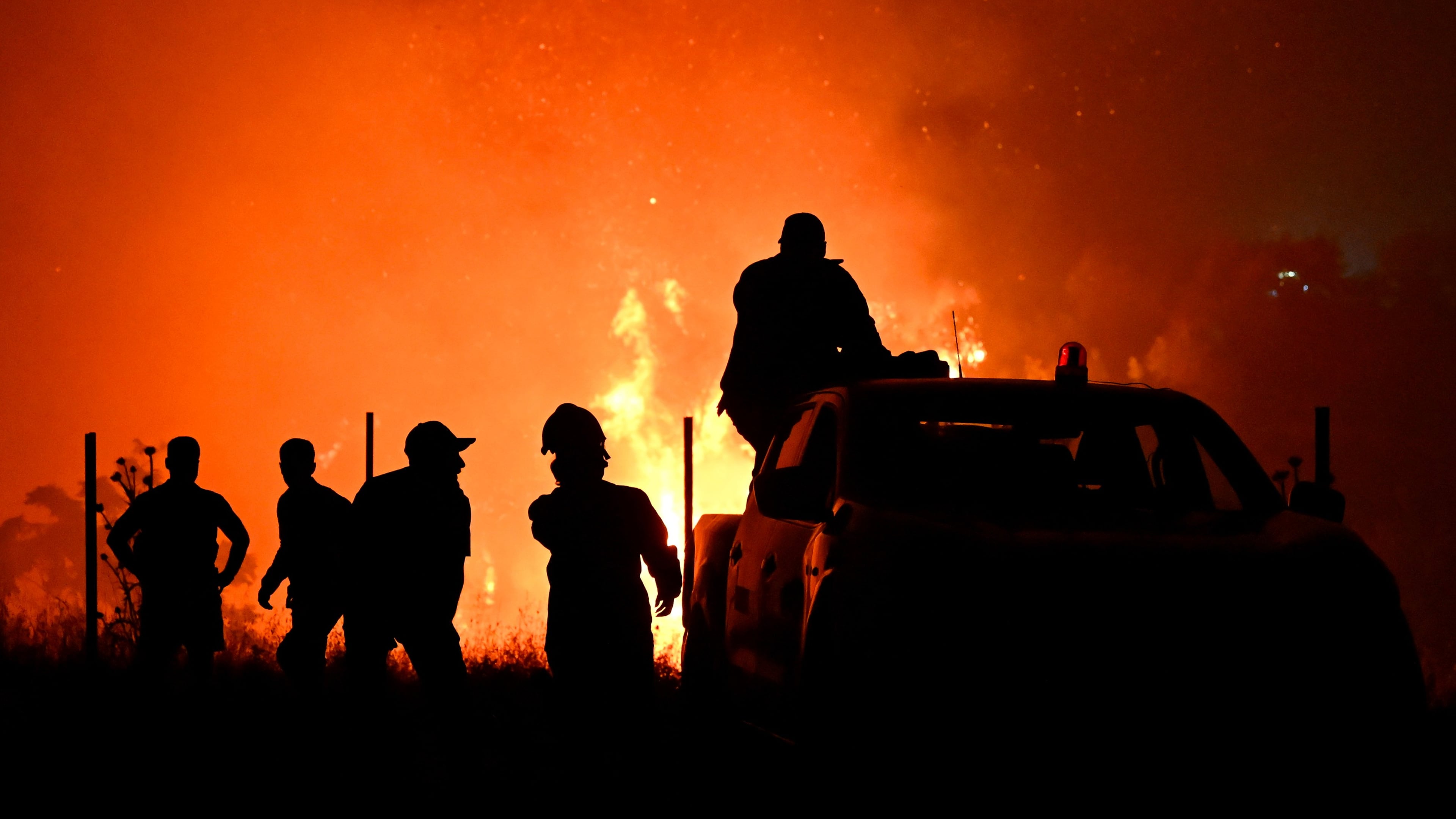 Firefighters and others are silhouetted in front of a wildfire on the outskirts of the northern city of Thessaloniki, Greece, Saturday, July 4, 2026. (AP Photo/Giannis Papanikos)