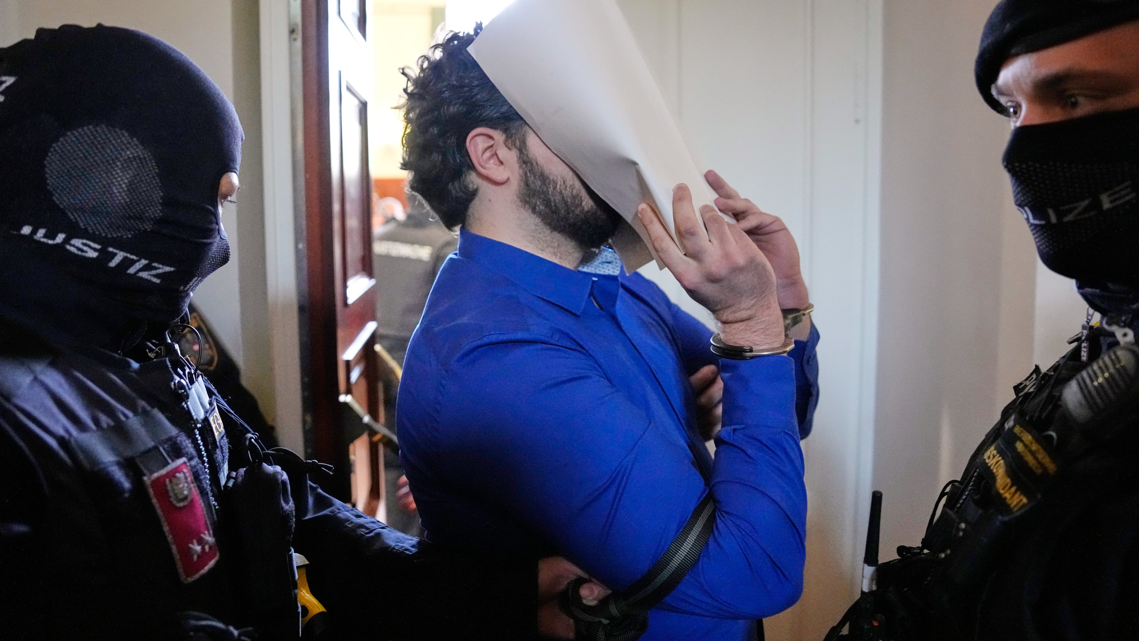 A defendant hiding his face behind file folders on the way to the courtroom in the District Court in Wiener Neustadt, Austria, where two terror suspects will stand trial Tuesday, one for plotting to carry out an attack on one of superstar singer Taylor Swift's concerts in Vienna in August 2024 and pledging allegiance to the Islamic State group, Tuesday, April 28, 2026. (AP Photo/Matthias Schrader)