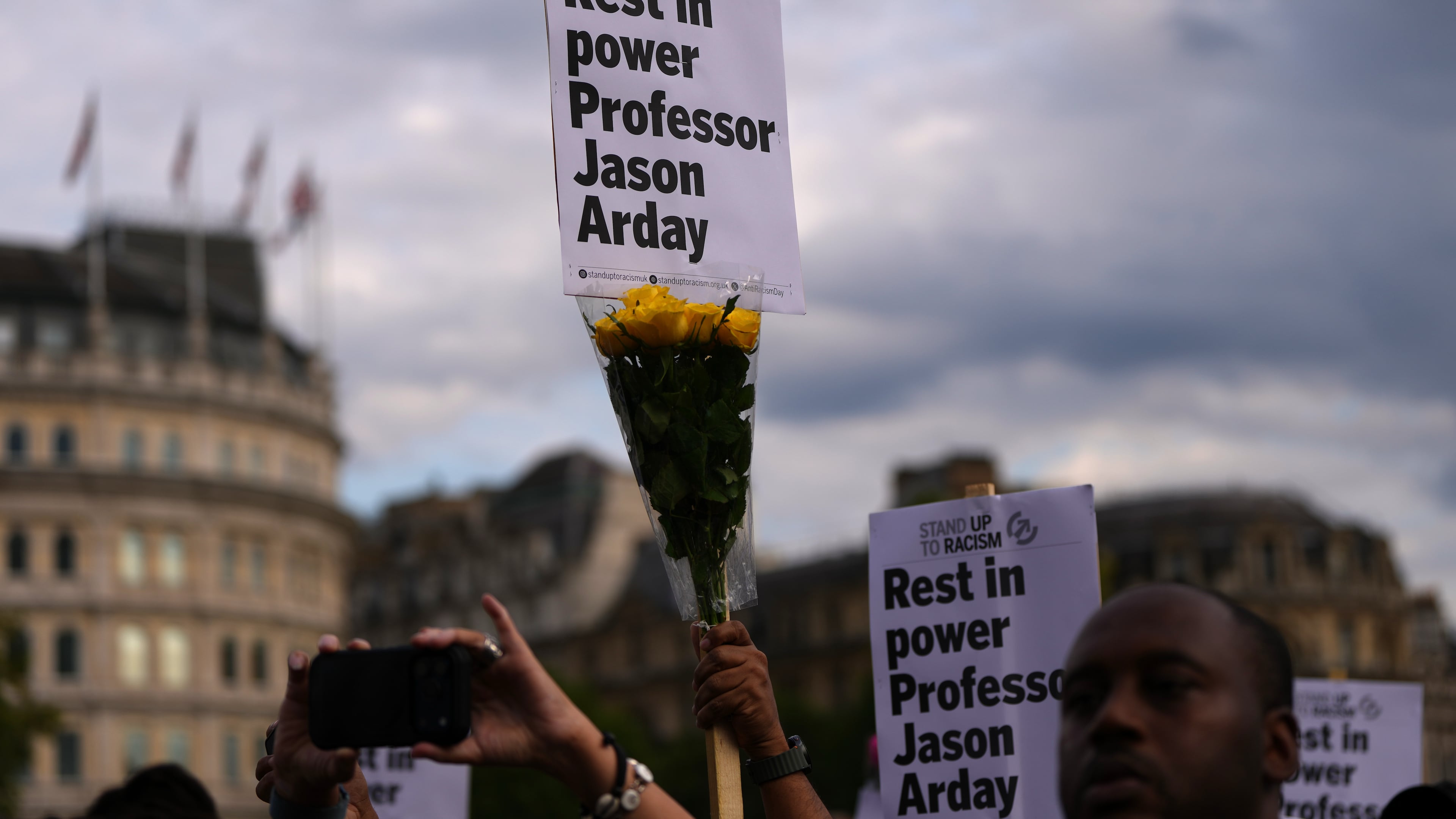 FILE - People attending a vigil held by Stand Up to Racism, in memory of late University of Cambridge professor Jason Arday, hold up signs at Trafalgar Square in London, on Aug. 17, 2026. (AP Photo/Kirsty Wigglesworth, File)