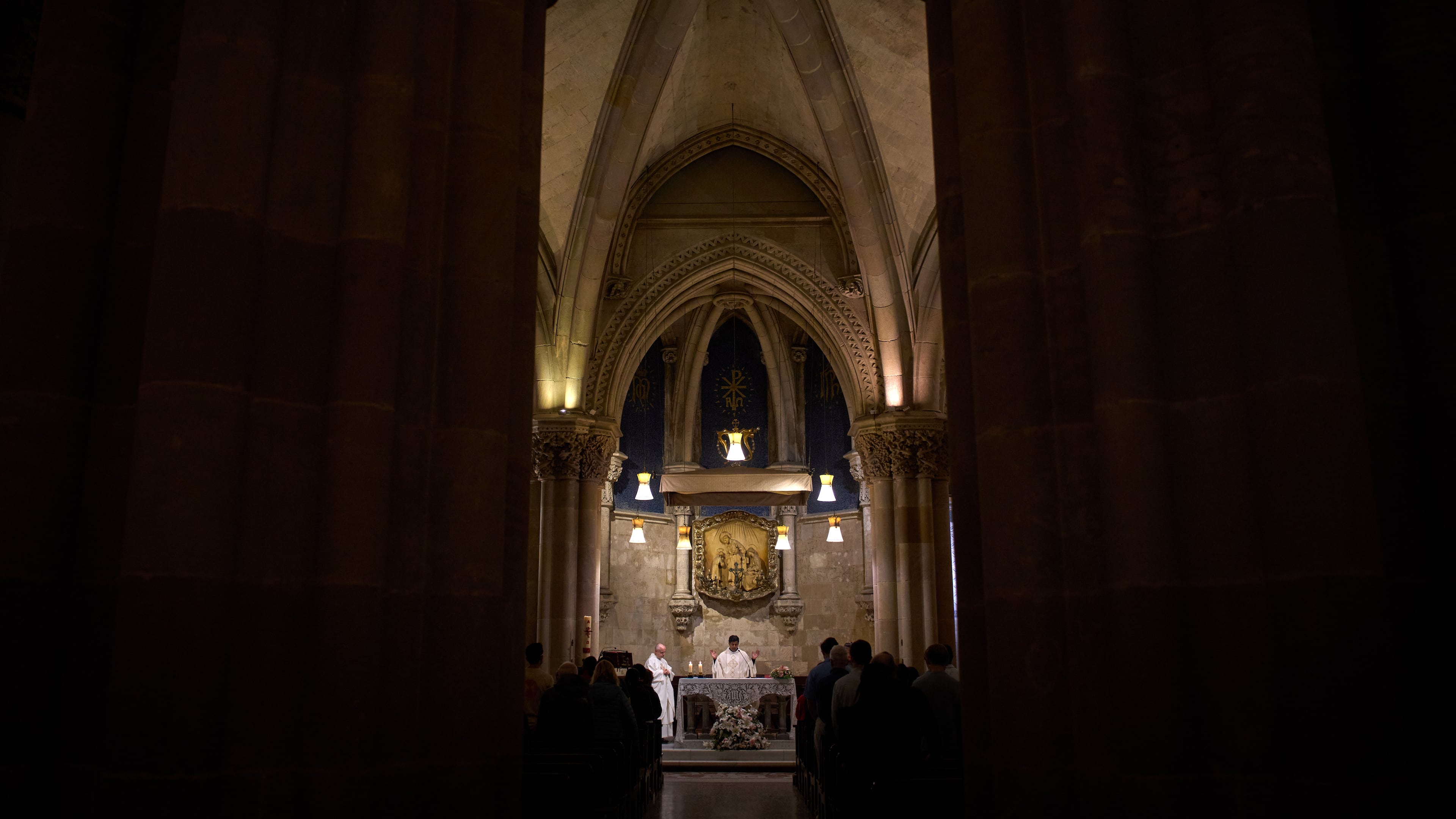 A priest celebrates Mass in the crypt of Antoni Gaudí beneath the Sagrada Familia while crowds of visitors fill the basilica above in Barcelona, Spain, May 15, 2026. (AP Photo/Emilio Morenatti)
