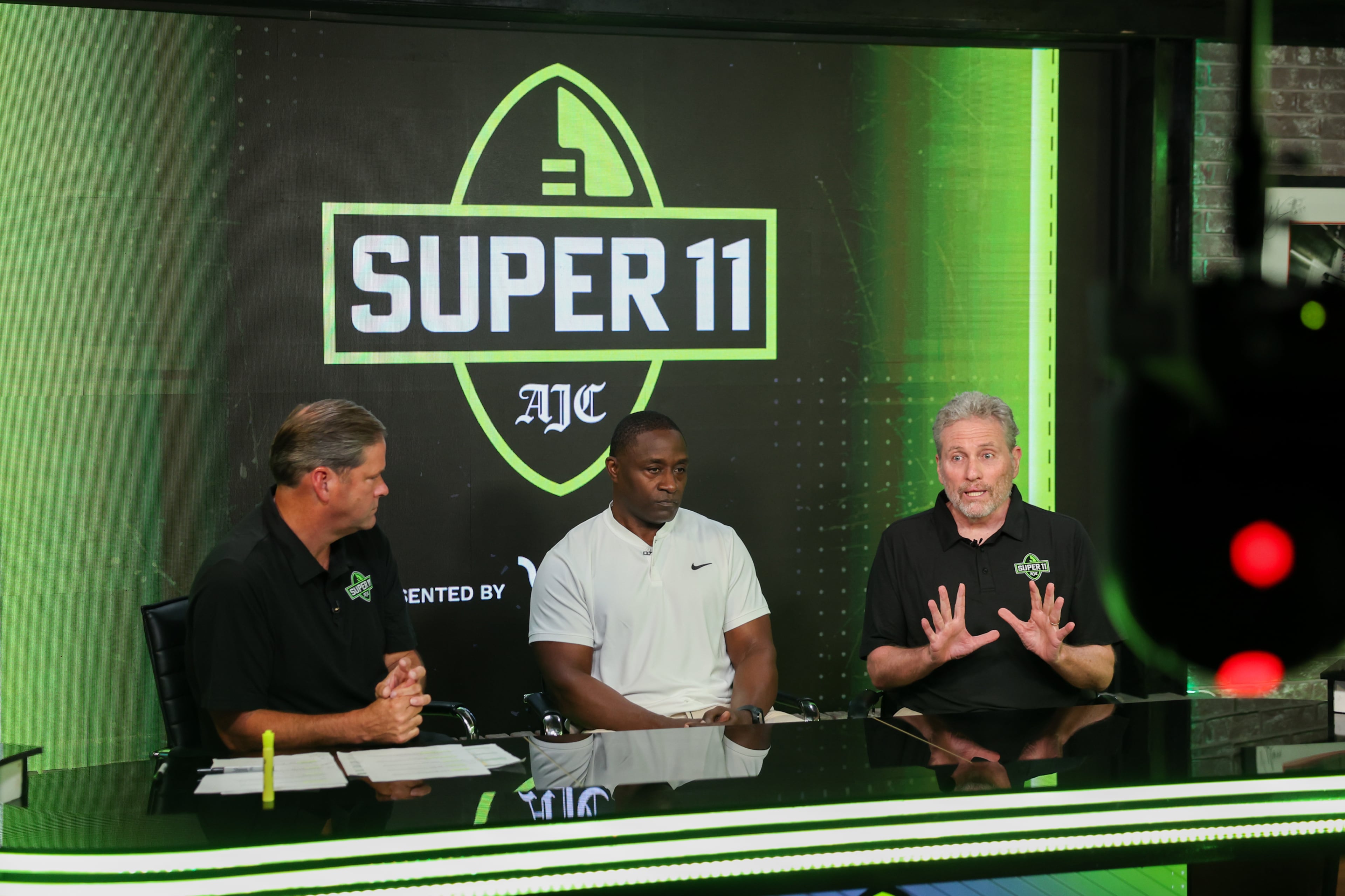 (L-R) DawgNation’s Brandon Adams appears with former Super 11 honoree Garrison Hearst and AJC’s Todd Holcomb during the taping of the Super 11 reveal show at Score ATL in Roswell on Aug. 3, 2026. (Arvin Temkar/AJC)