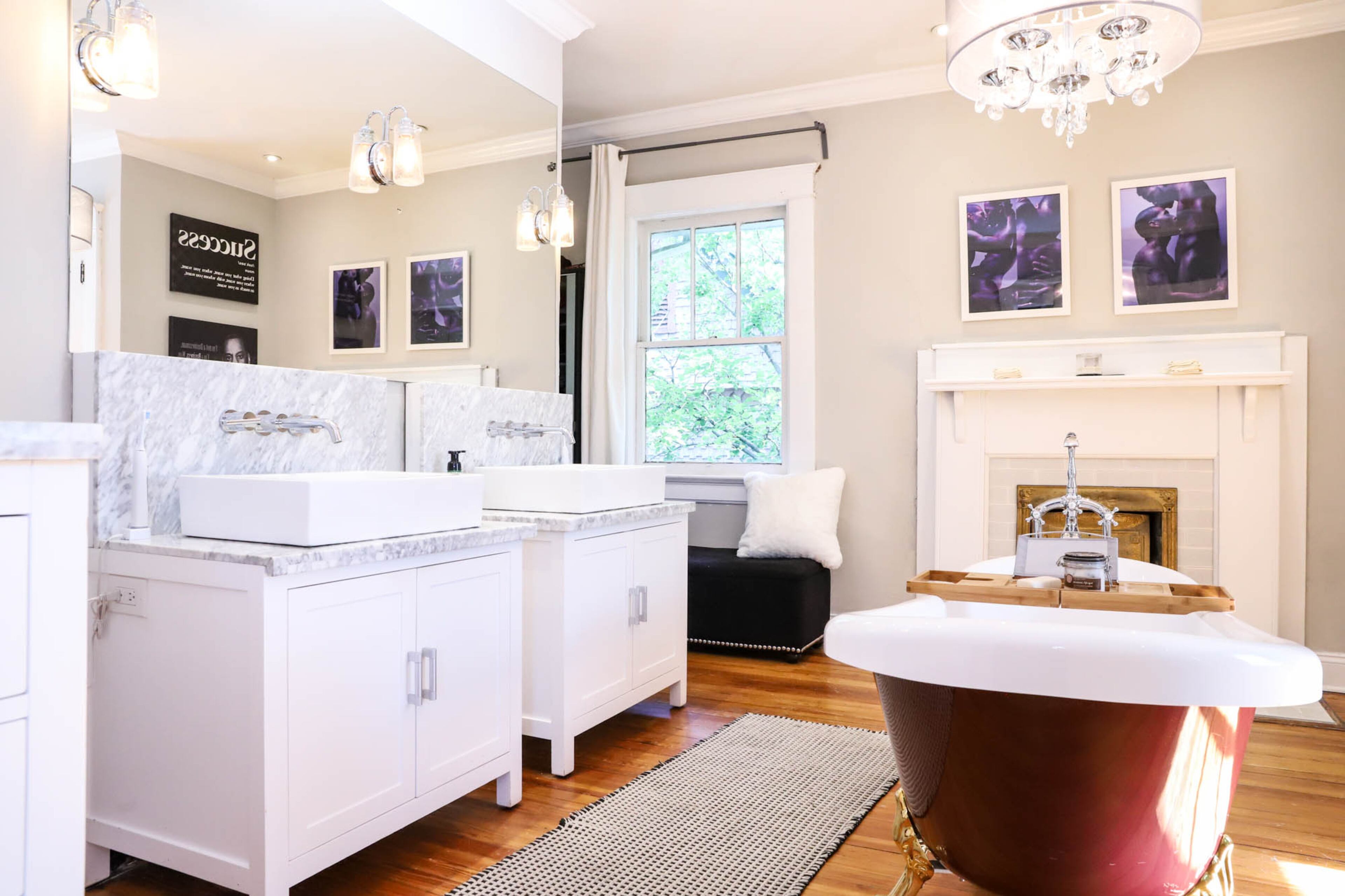 A luxurious bath sits right off of Larry and Antoine Carter’s bedroom in their Historic West End home. Original hardwoods and an original fireplace set a vintage tone matched by the clawfoot bathtub in the center of the space, but two bright white vanities from Overstock.com and a chic chandelier give the room more contemporary touches. Above the fireplace hang two photos of Antoine and Larry taken by photographer James C. Lewis printed on metal sheets. Text by Shannon Dominy/Photo by Reynolds Rogers