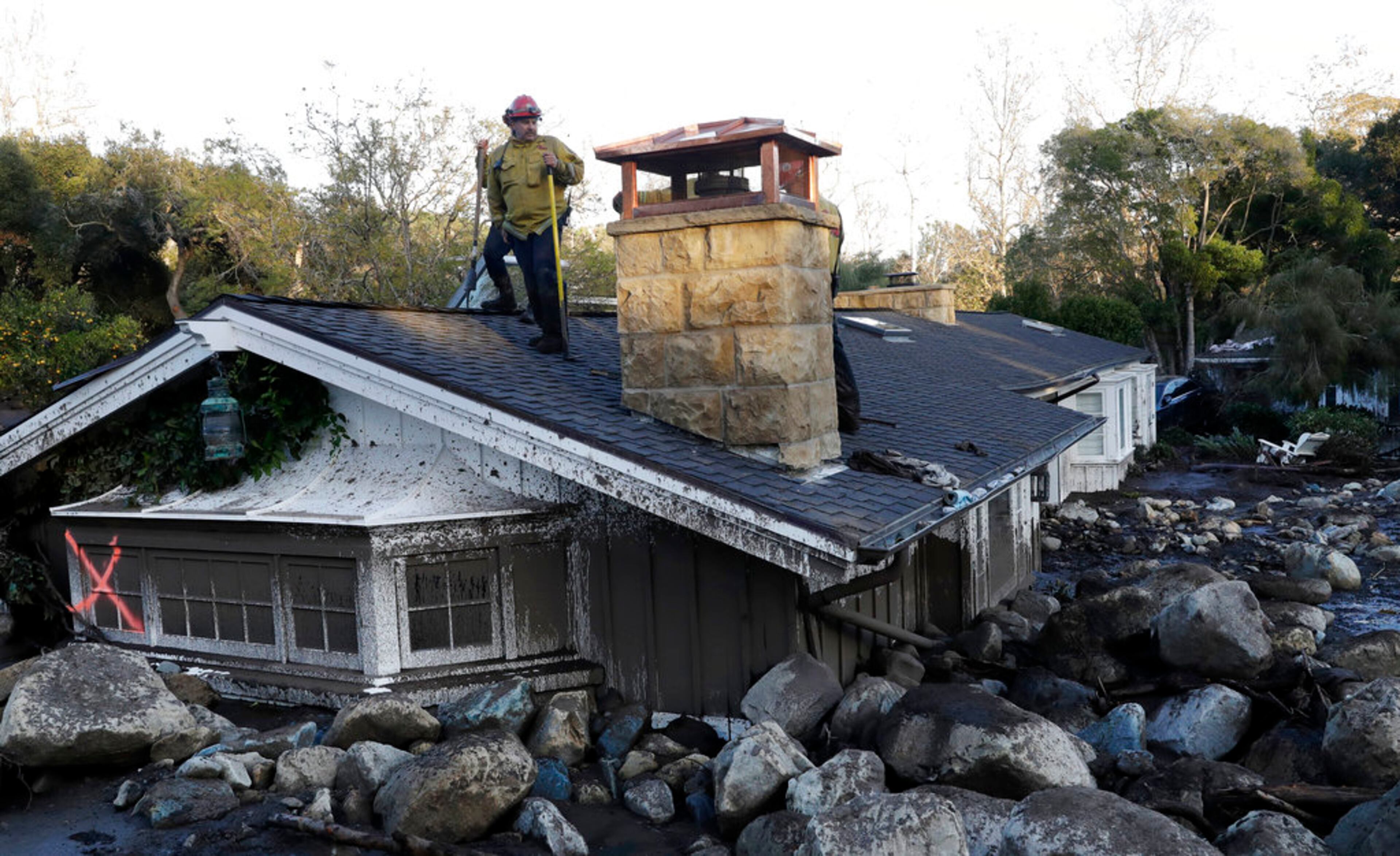 A firefighter stands on the roof of a house submerged in mud and rocks Wednesday, Jan. 10, 2018, in Montecito, Calif. Anxious family members awaited word on loved ones Wednesday as rescue crews searched grimy debris and ruins for more than a dozen people missing after mudslides in Southern California destroyed houses, swept cars to the beach and left more than a dozen victims dead. (AP Photo/Marcio Jose Sanchez)