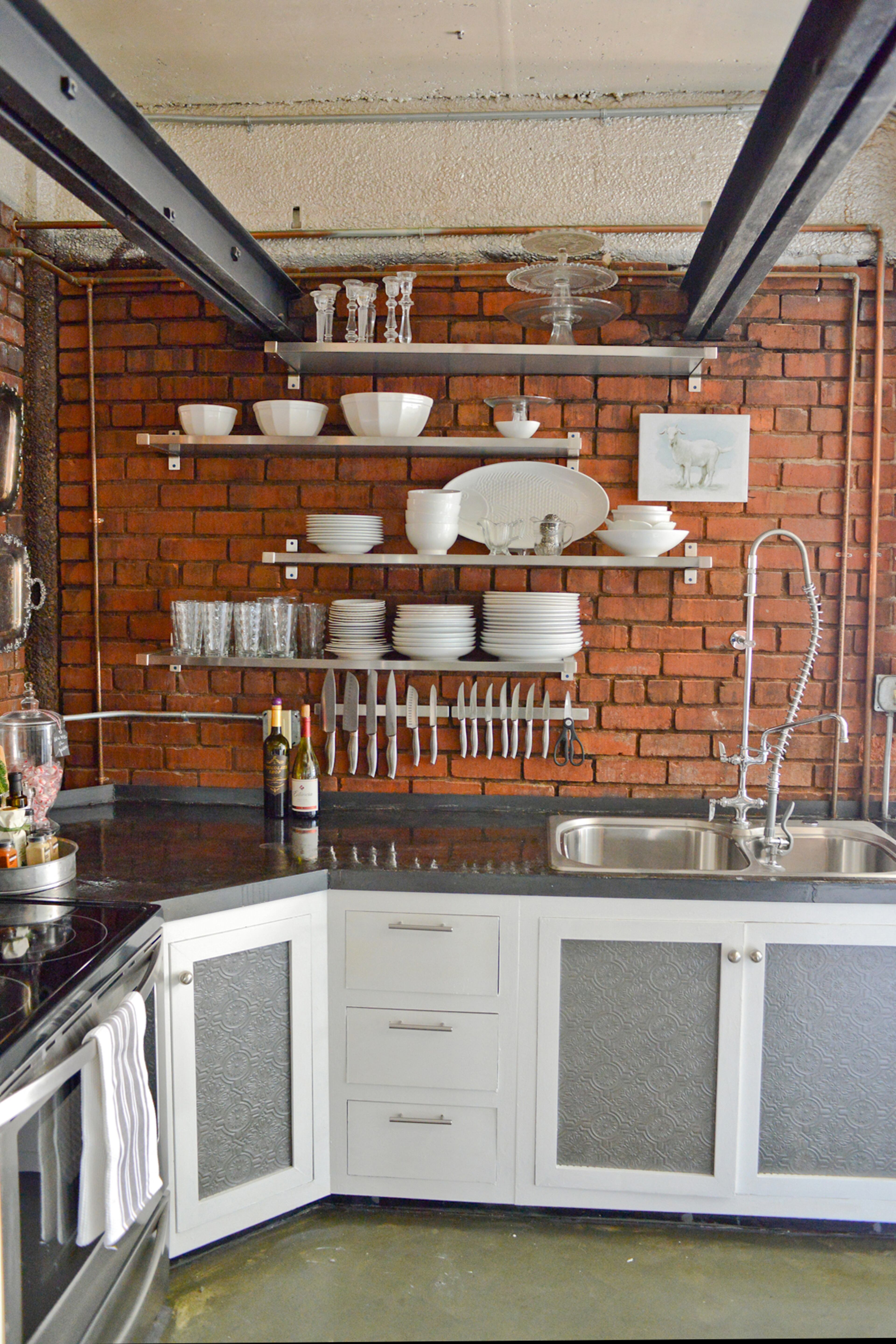 All of the brickwork in the kitchen is original to the nearly 90-year-old building. The kitchen is the former elevator shaft of a meatpacking factory in Atlanta and now the space has concrete countertops, open metal shelving and white cabinets with a painted inlay that looks like vintage tin.