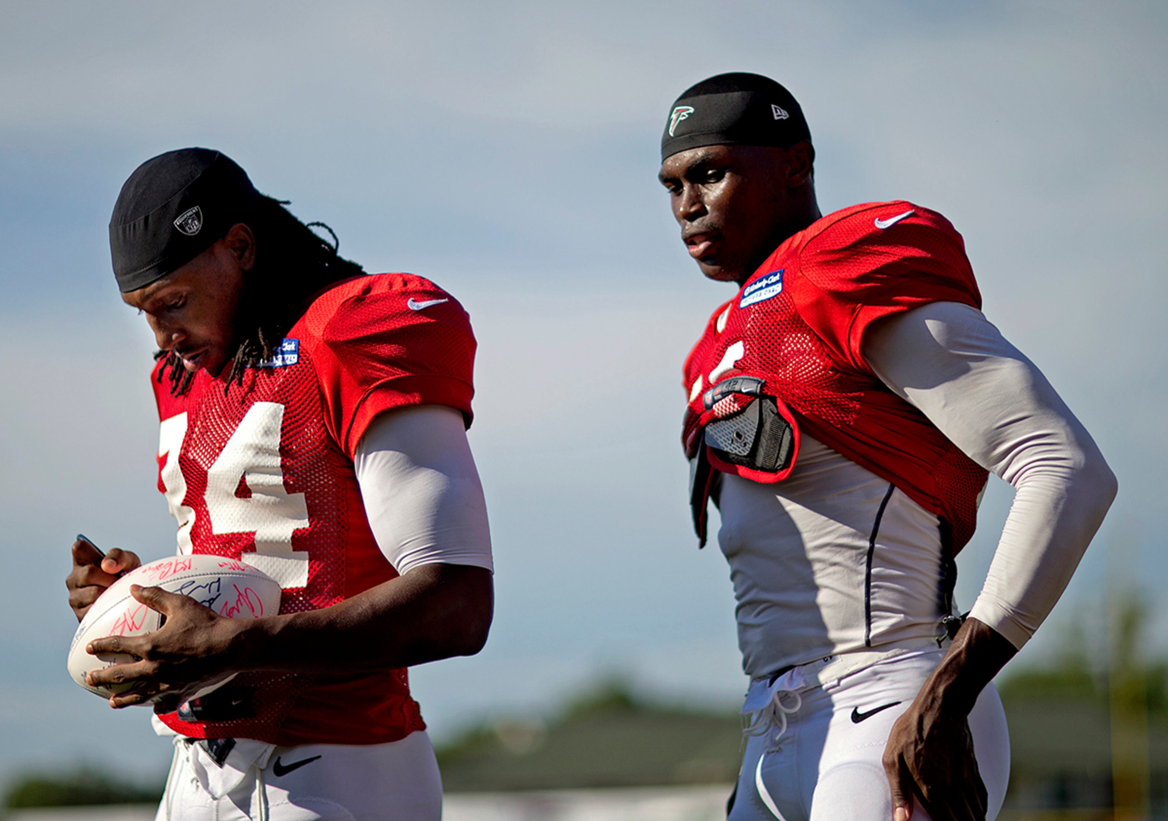 Falcons wide receiver Roddy White (left) autographs a football while leaving the field with teammate Julio Jones Monday following practice during training camp at the team's practice facility in Flowery Branch.