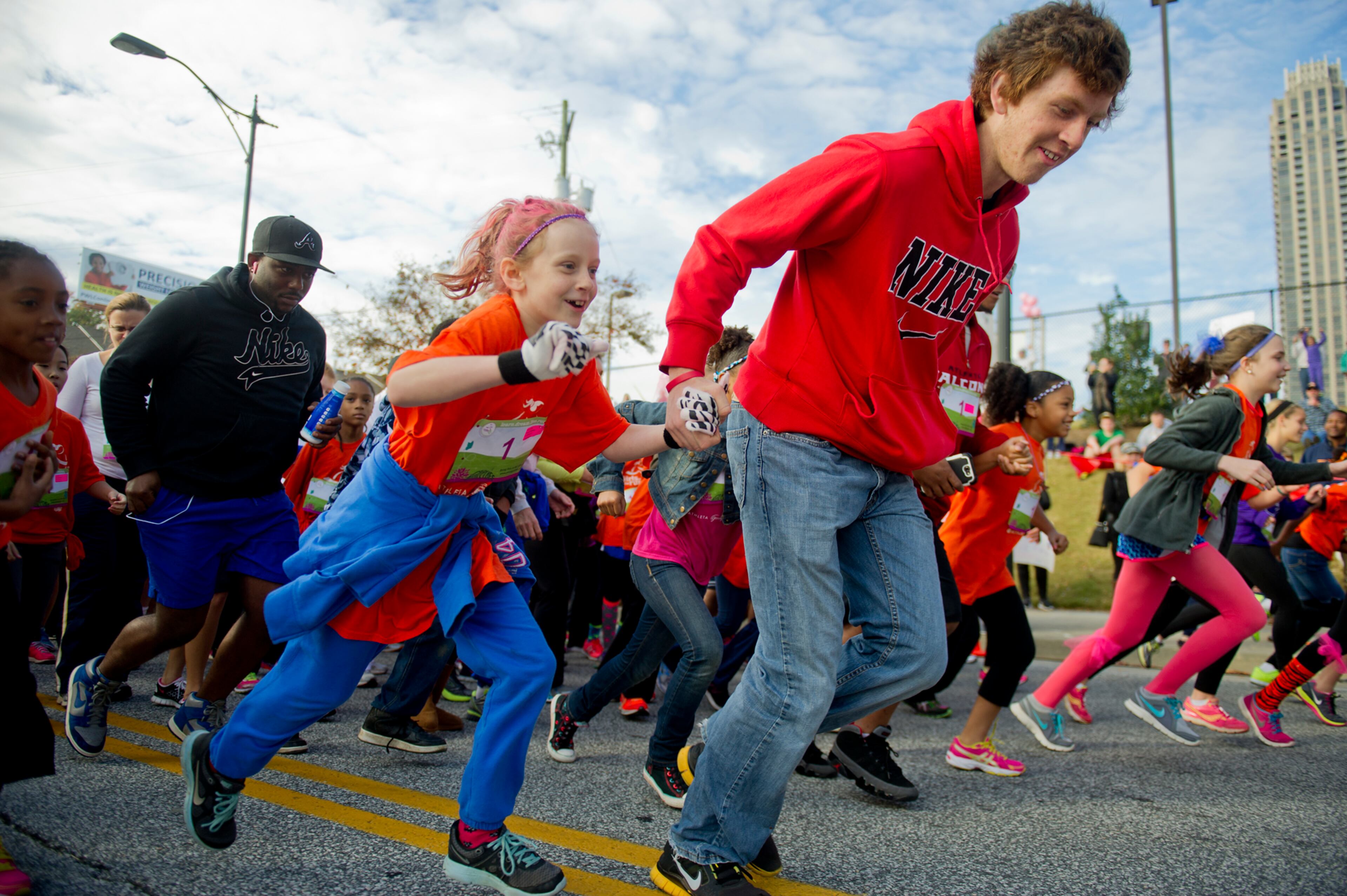 Faith Covey (left) holds hands with her brother Nick as they take off from the starting line during the 2013 Girls on the Run 5K at Atlantic Station in Atlanta on Nov. 10, 2013.