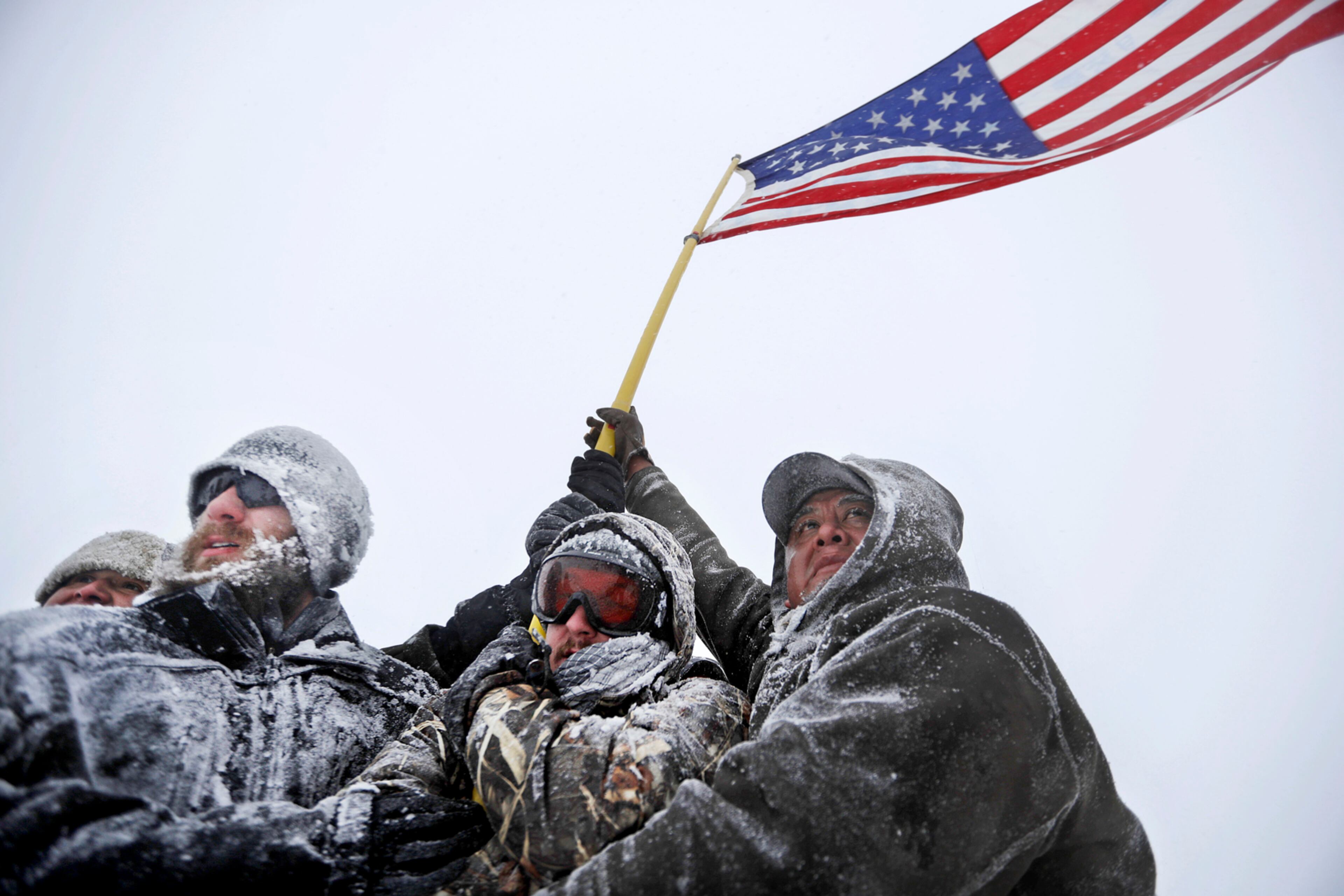 Military veterans huddle together to hold a United States flag against strong winds during a march to a closed bridge outside the Oceti Sakowin camp where people have gathered to protest the Dakota Access oil pipeline in Cannon Ball, N.D., Monday, Dec. 5, 2016. (AP Photo/David Goldman)