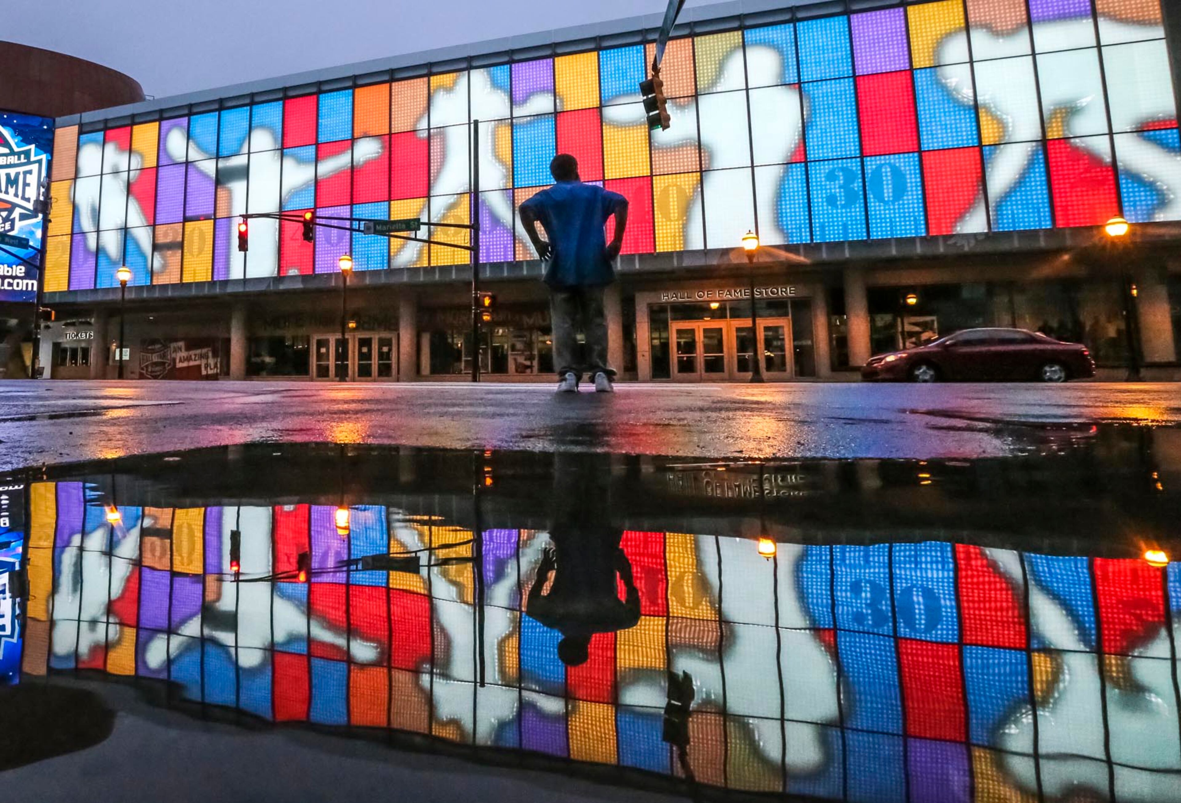 June 22, 2017 Atlanta: Kenny Brown walks by the pooling water from rain reflected the colorful facade of the College Football Hall of Fame at 250 Marietta St NW, in downtown Atlanta on Thursday, June 22, 2017. JOHN SPINK/JSPINK@AJC.COM.