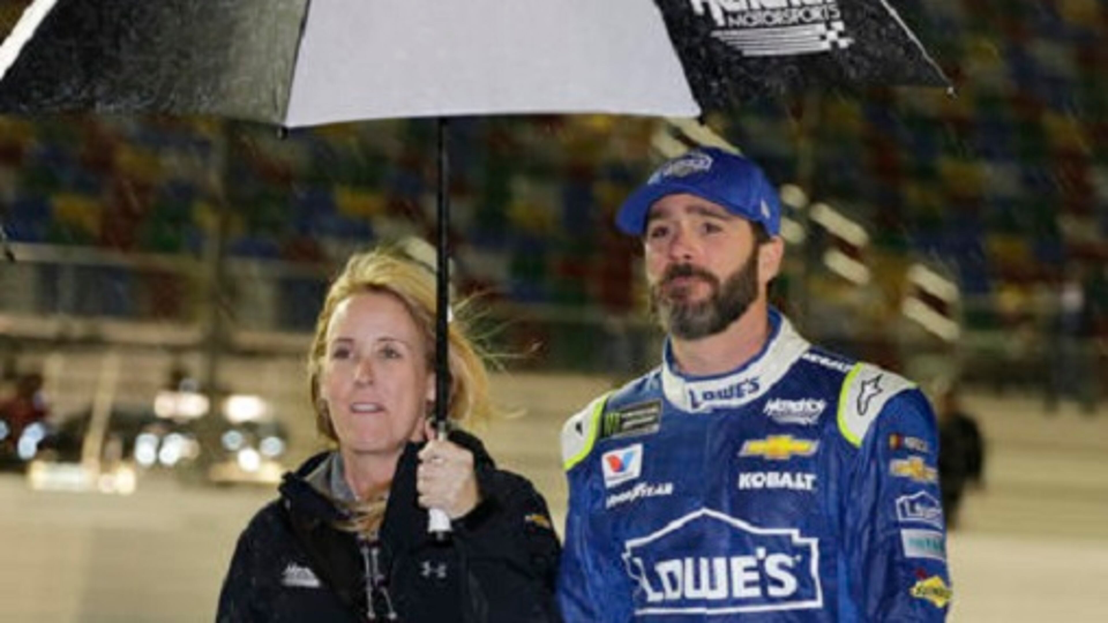 Jimmie Johnson, right, takes shelter under an umbrella with a team member during a rain delay before the NASCAR Clash auto race at Daytona International Speedway, Saturday, Feb. 18, 2017, in Daytona Beach, Fla. (AP Photo/Terry Renna)