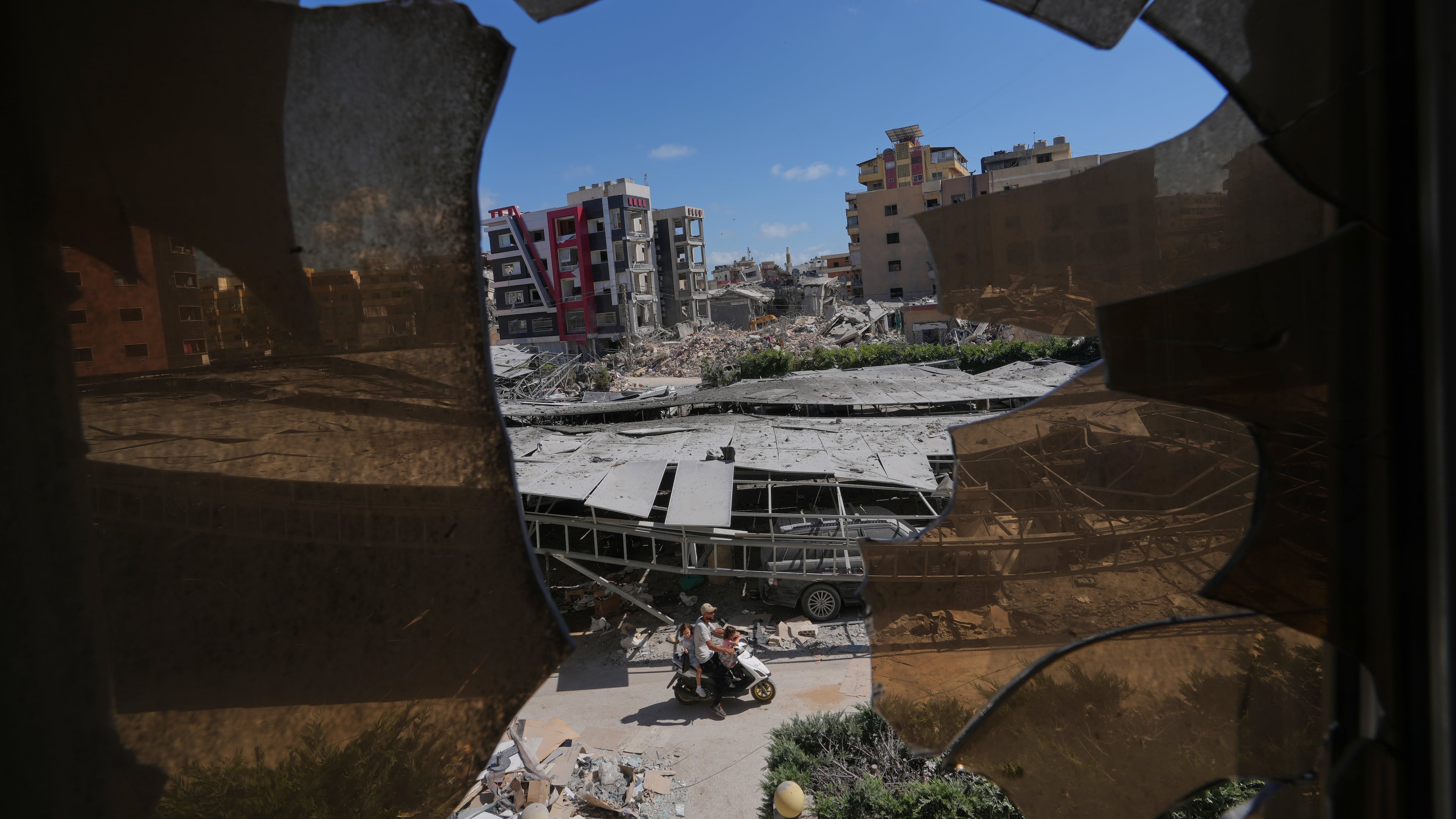 Buildings damaged by Israeli strikes are seen through shattered glass from the Jabal Amel Hospital in the southern port city of Tyre, Lebanon, Thursday, June 18, 2026. (AP Photo/Hassan Ammar)