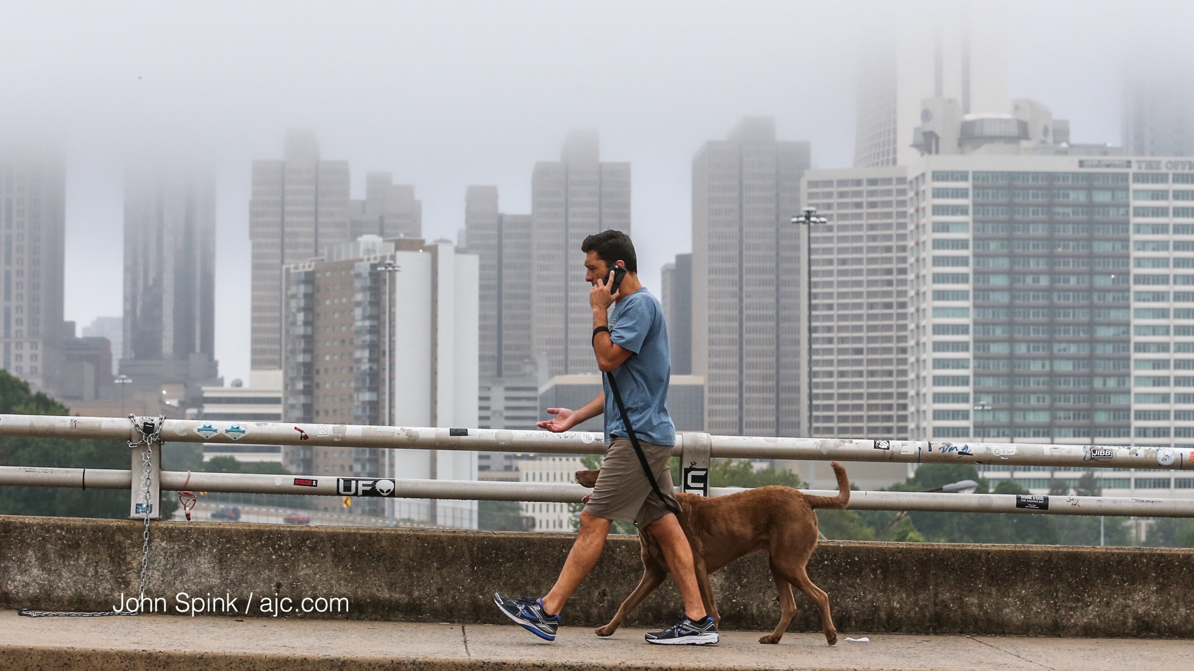 Chris Salomone walks his dog along the Jackson Street bridge against a foggy Atlanta skyline. JOHN SPINK / JSPINK@AJC.COM