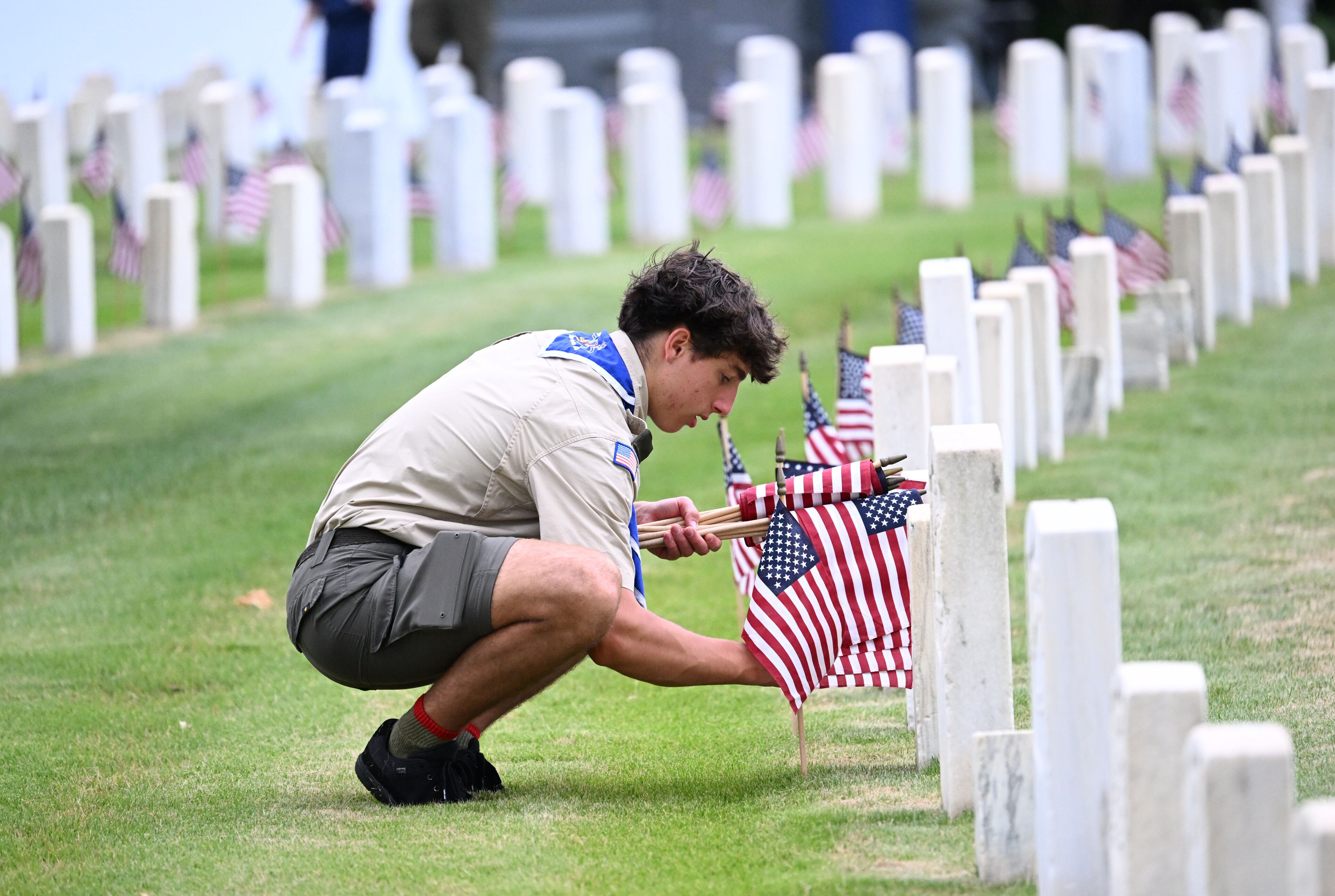 Conner Clark places a flag in front of a headstone during the Memorial Day Flag Placement event at Marietta National Cemetery on Saturday, May 23, 2026, in Marietta. Scouting groups in the community place more than 18,000 U.S. veteran grave flags at Marietta National Cemetery each year on the Saturday before Memorial Day, helping prepare for Monday’s ceremony. The long-running service project—organized with the National Memorial Day Association of Georgia—also gives youth and adults an opportunity to honor fallen service members and learn about their sacrifices and the area’s history. (Hyosub Shin/AJC)