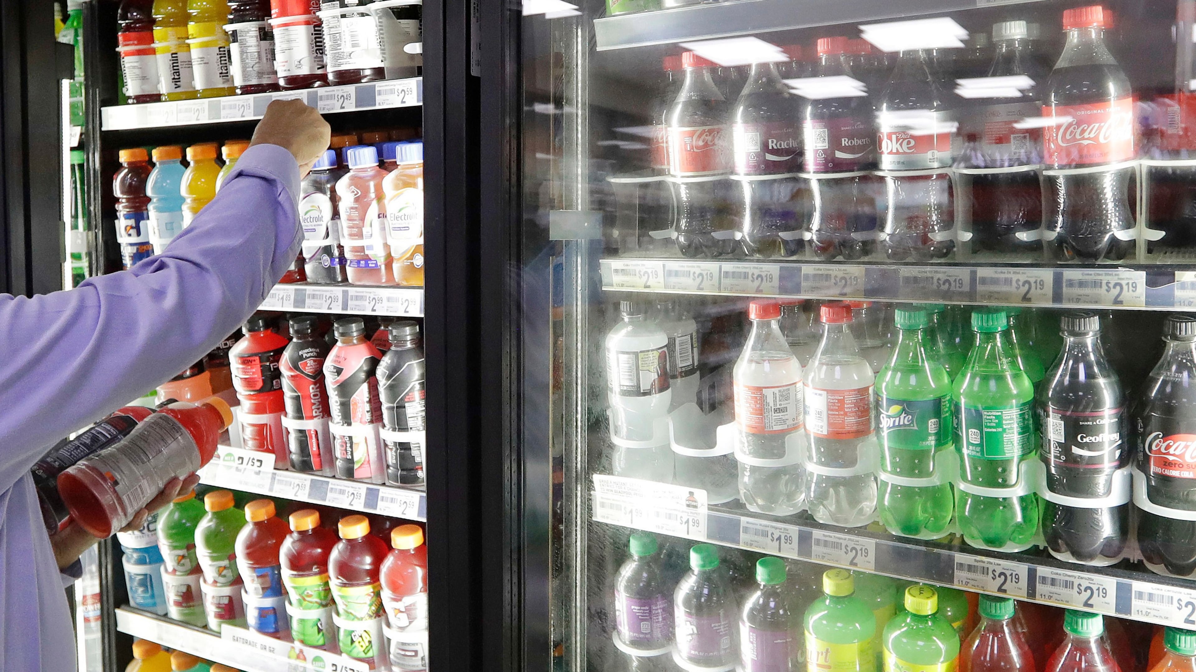 FILE - A shop owner reaches into a drink display refrigerator at his convenience store in Kent, Wash., Oct. 1, 2018. (AP Photo/Elaine Thompson, File)