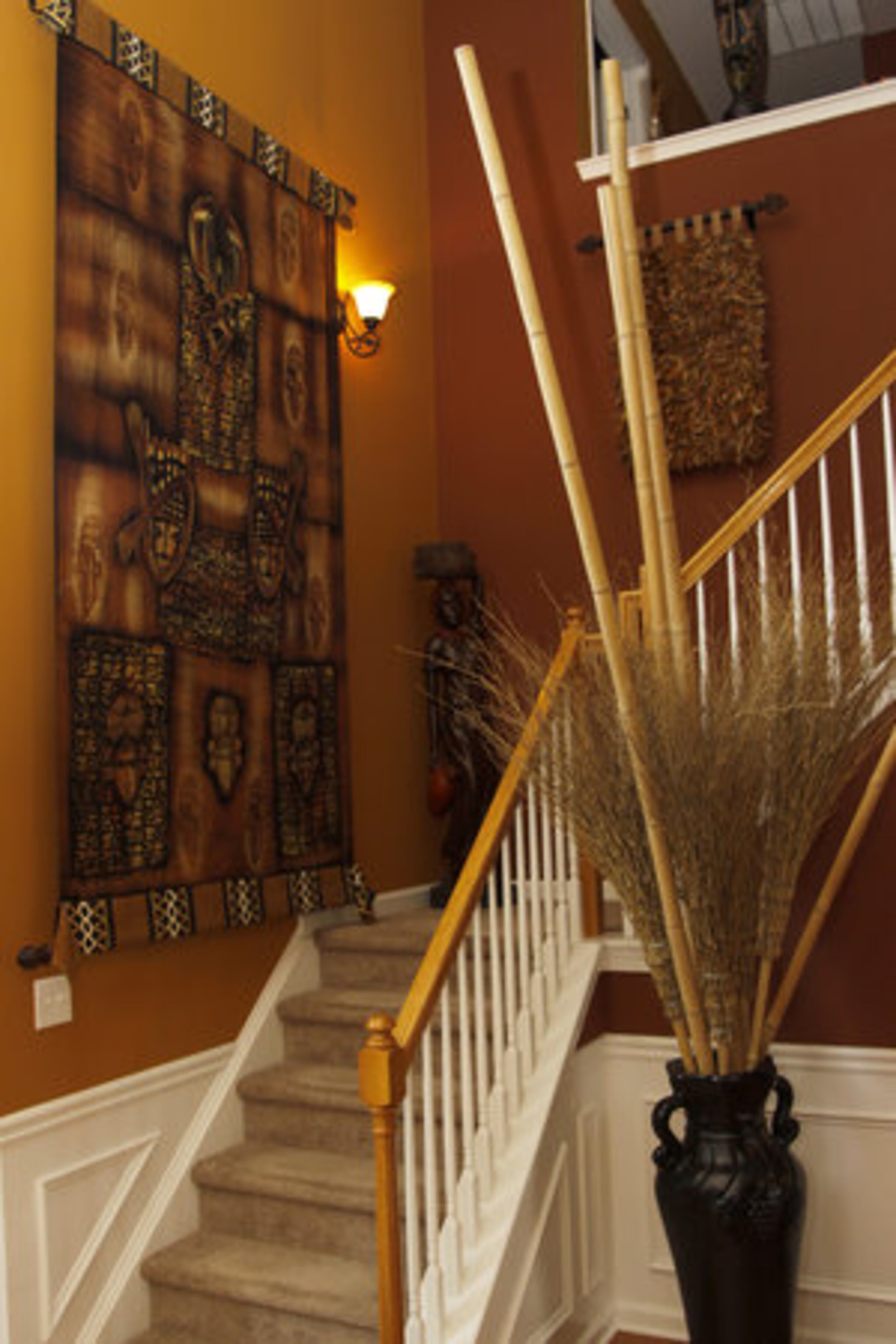 The eye-catching tapestry draped on a wall at the staircase near the foyer is from Africa and bears depictions of strong soldiers. DeCuir demonstrates how cheap can be chic by filling a tall vase with real bamboo rods and five "witches brooms" he sourced at Big Lots!