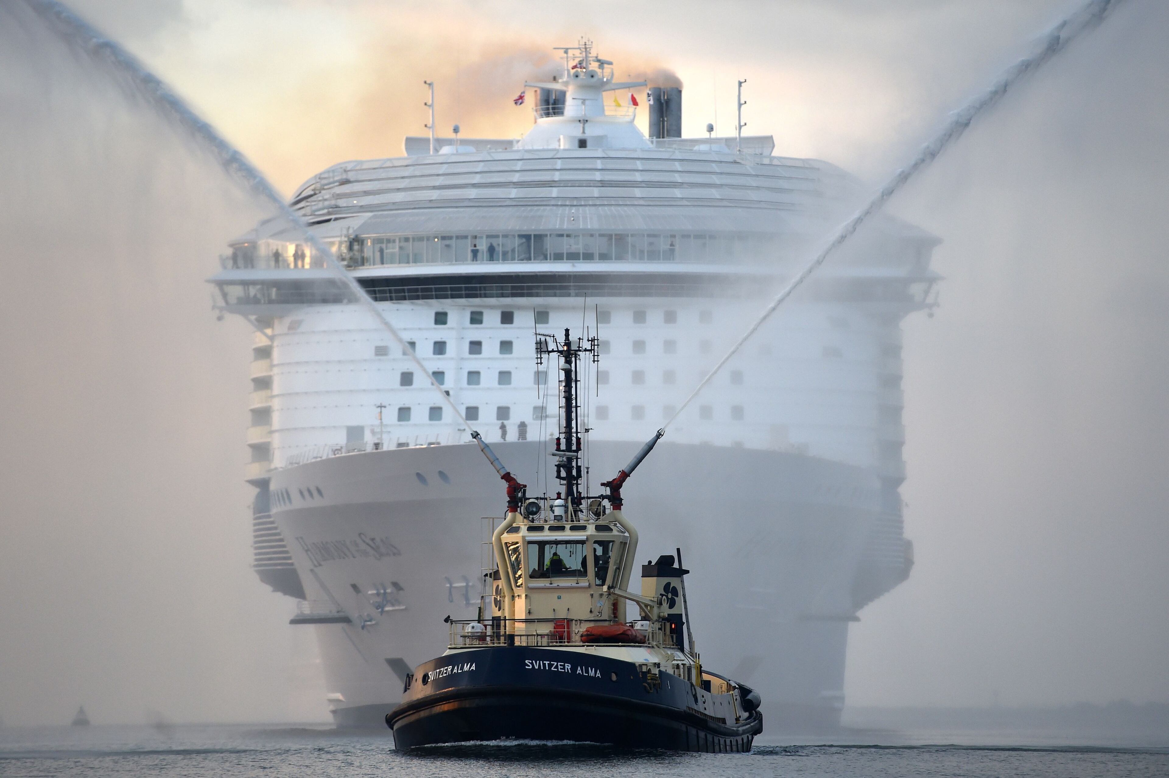 A tug boat leads the way for the world's largest passenger ship, Harmony of the Seas, owned by Royal Caribbean, as it makes her way up Southampton Water, into Southampton, England, Tuesday May 17, 2016, ahead of her maiden cruise. After 32-months being fitted out in a French shipyard the 16-deck Harmony of the Seas will set out on its inaugural voyage on May 22 bound for Barcelona, Spain. (Andrew Matthews/PA via AP)