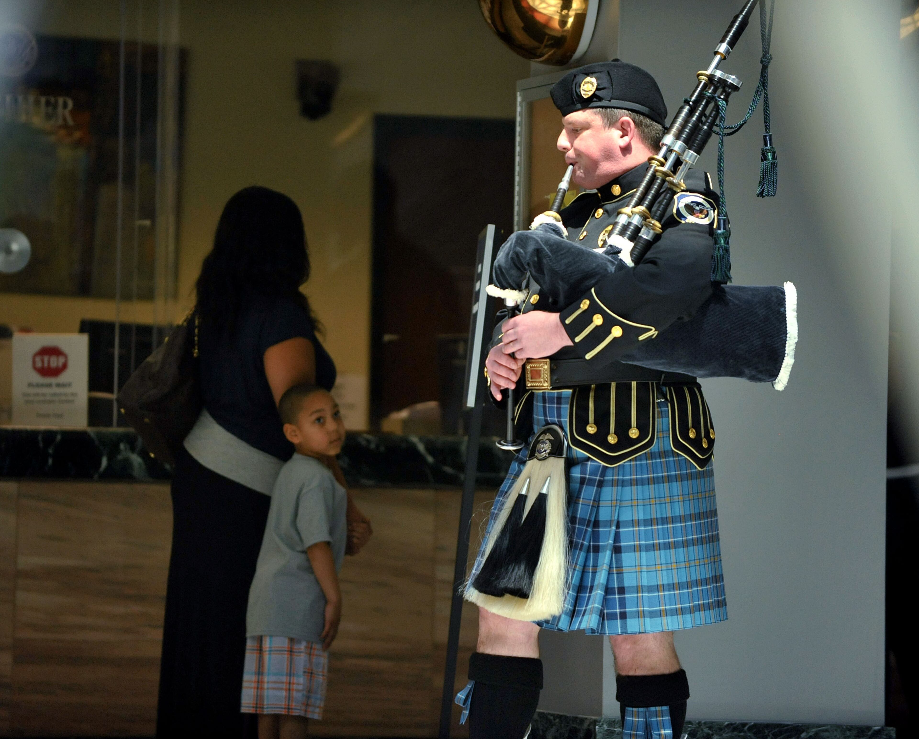 As a small child looks on, bagpiper Tommy Burns with the Cobb County Police Department, plays a musical selection during the service in which the Atlanta Police Department recognized 82 fallen officers on Tuesday, May 5, 2015. KENT D. JOHNSON /KDJOHNSON@AJC.COM