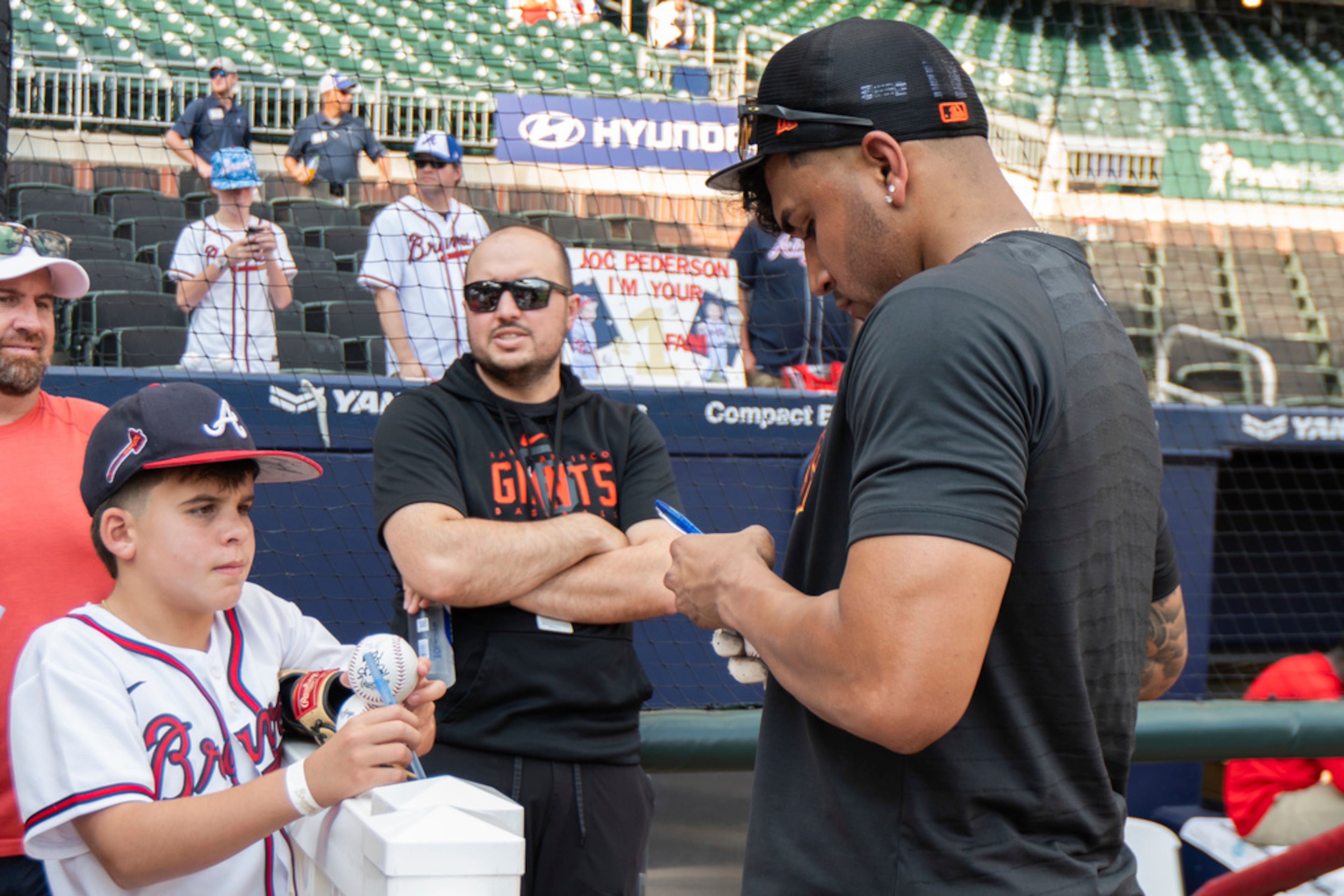 San Francisco Giants' third baseman Johan Camargo, right, autographs a ball for a fan before a baseball game against the Atlanta Braves, Friday, Aug. 18, 2023, in Atlanta. (AP Photo/Hakim Wright Sr.)