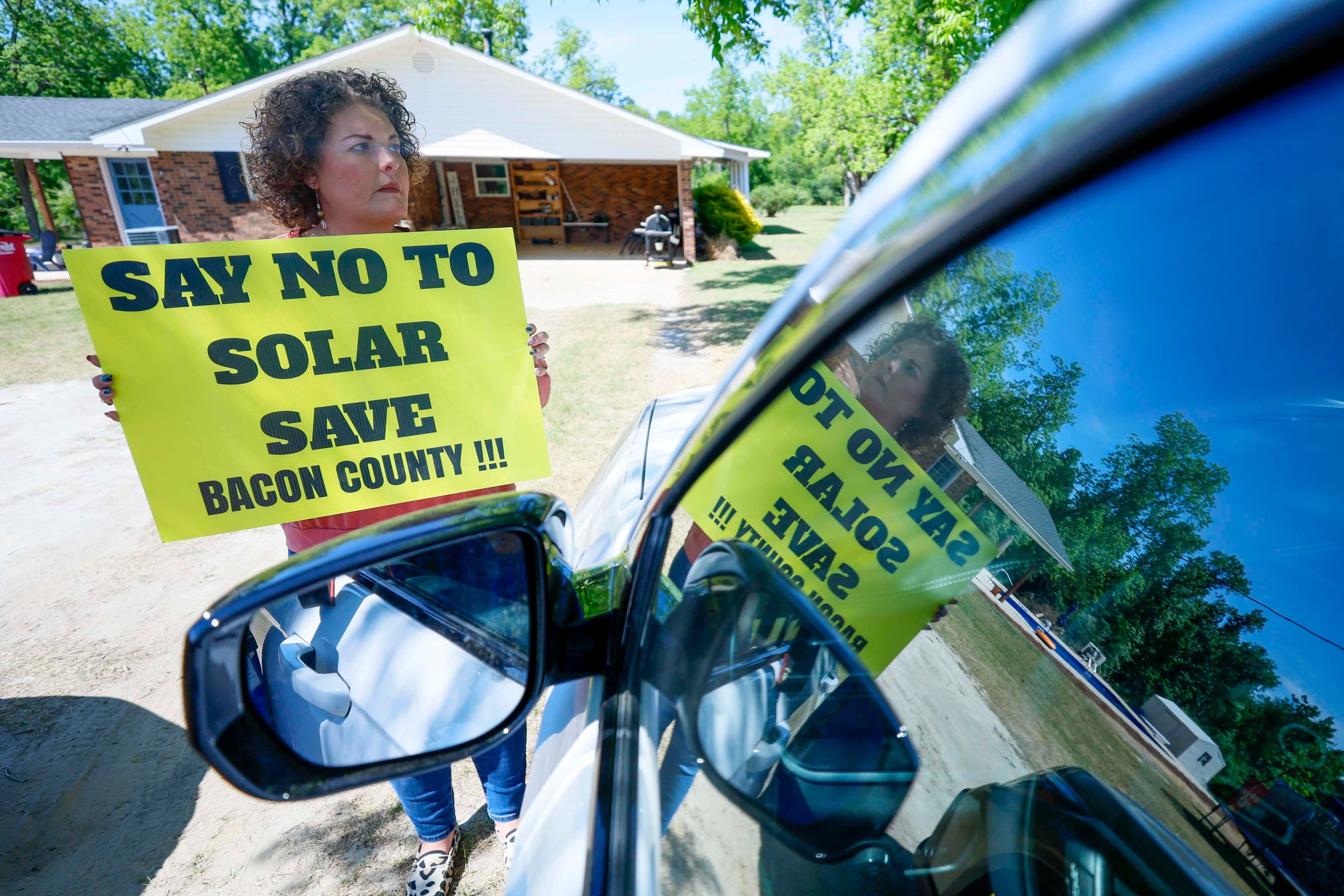 Shea Hutchinson, a local resident and candidate for the Bacon County commission, is holding a sign opposing the construction site where Silicon Ranch is building one of the state’s largest solar farms outside Alma, Ga., on Tuesday, April 21, 2026. She has voiced her opposition at every board meeting she has attended. (Miguel Martinez/AJC)