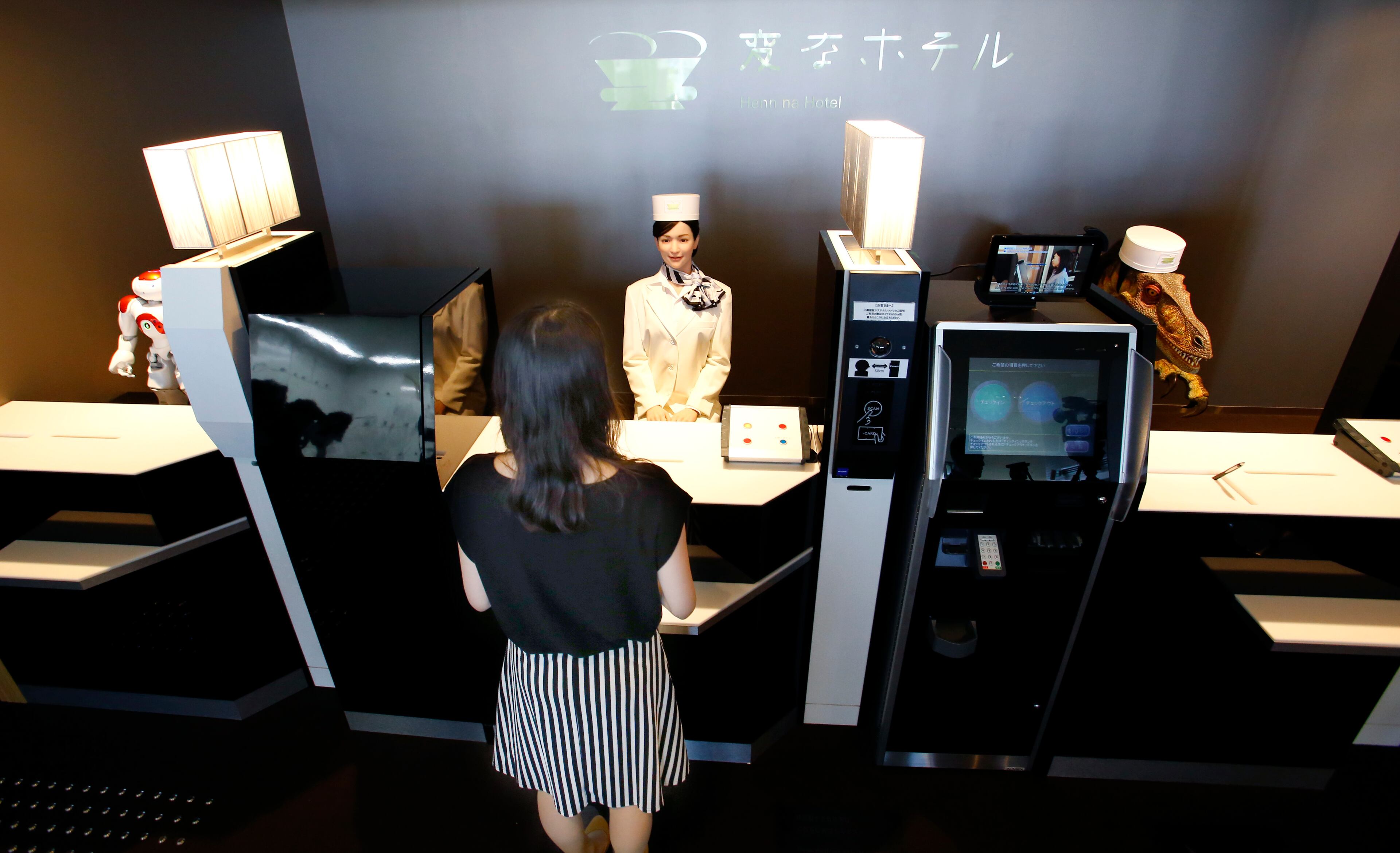 A receptionist robot, top center, accompanied by two other robots, greets a hotel employee demonstrating how to check in the new hotel, aptly called Henn na Hotel or Weird Hotel, in Sasebo, southwestern Japan, Wednesday, July 15, 2015. From the receptionist that does the check-in and check-out to the porter that's a stand-on-wheels taking luggage up to the room, the hotel, that is run as part of Huis Ten Bosch amusement park, is "manned" almost totally by robots to save labor costs. (AP Photo/Shizuo Kambayashi)