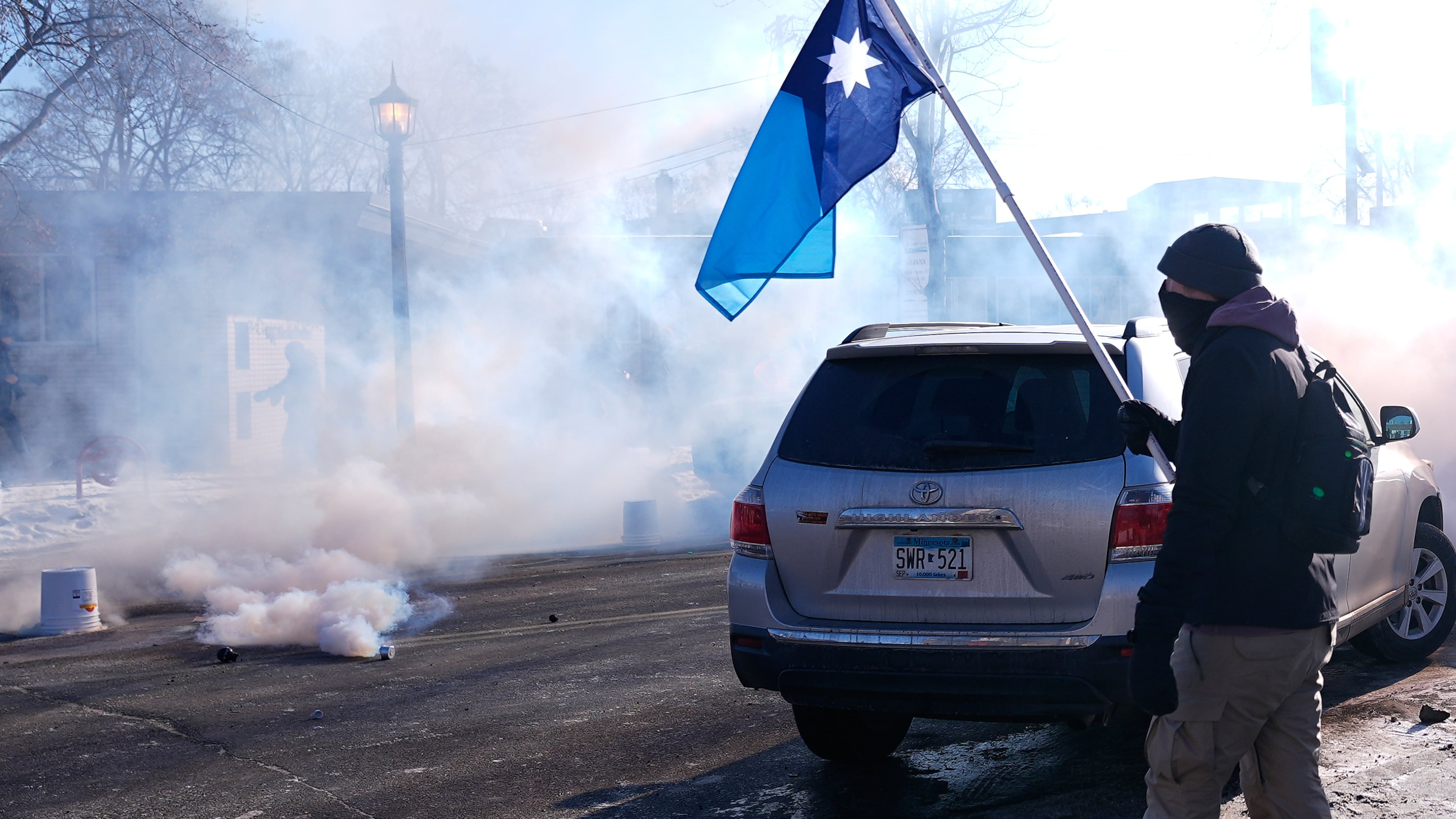 A person holds a Minnesota state flag as federal immigration officers deploy tear gas Saturday, Jan. 24, 2026, in Minneapolis. (AP Photo/Abbie Parr)