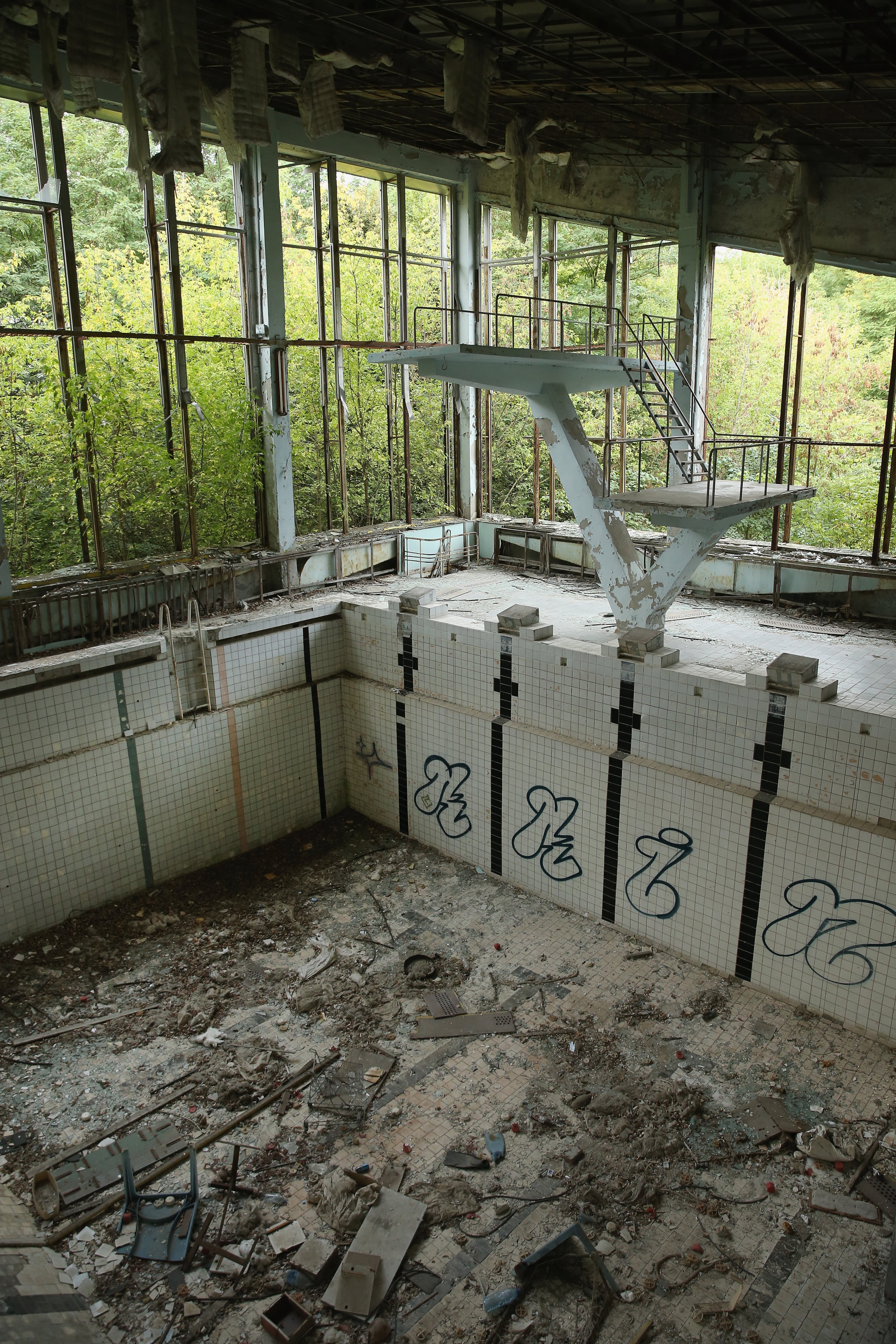 PRIPYAT, UKRAINE - SEPTEMBER 30: Diving boards stand over the remains of a pool at the abandoned "Lazurna" public swimming pools facility on September 30, 2015 in Pripyat, Ukraine. Pripyat lies only a few kilometers from the former Chernobyl nuclear power plant and was built in the 1970s to house the plant's workers and their families. On April 26, 1986, technicians at Chernobyl conducting a test inadvertently caused reactor number four to explode, sending plumes of highly radioactive particles and debris into the atmosphere. Authorities evacuated 120,000 people from the area, including 43,000 from Pripyat. Today Pripyat is a ghost-town, its apartment buildings, shops, restaurants, hospital, schools, cultural center and sports facilities derelict and its streets overgrown with trees. The city lies in the inner exclusion zone around Chernobyl where hot spots of persistently high levels of radiation make the area uninhabitable for thousands of years to come. (Photo by Sean Gallup/Getty Images)