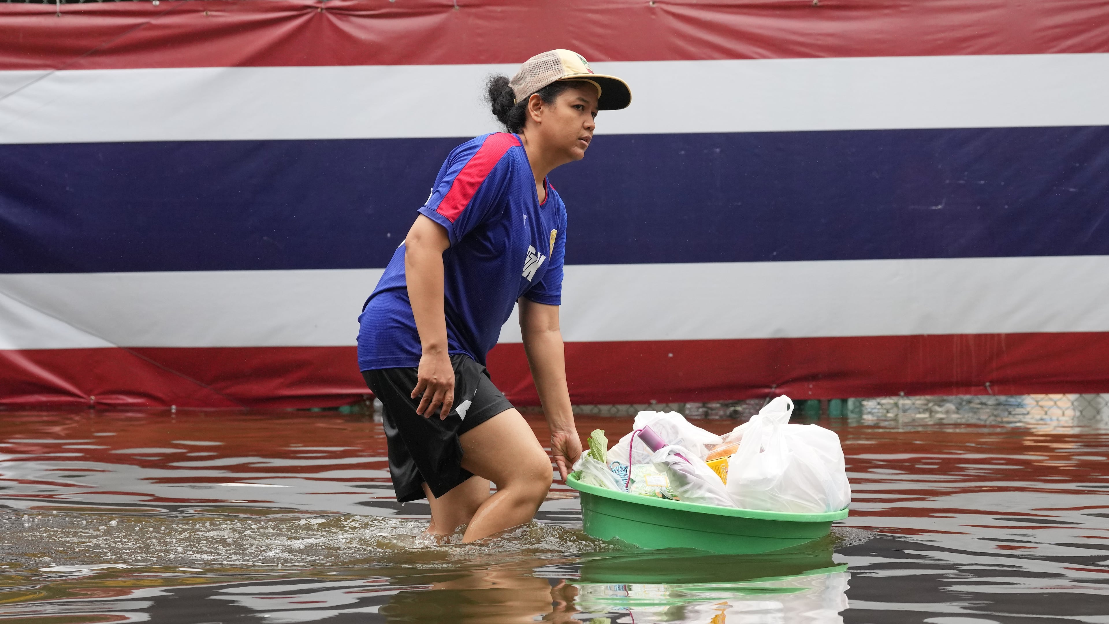 A woman wades through floodwaters in front of a national flag after heavy rain in Bangkok, Thailand, Sunday, Sept. 27, 2026. (AP Photo/Sakchai Lalit)