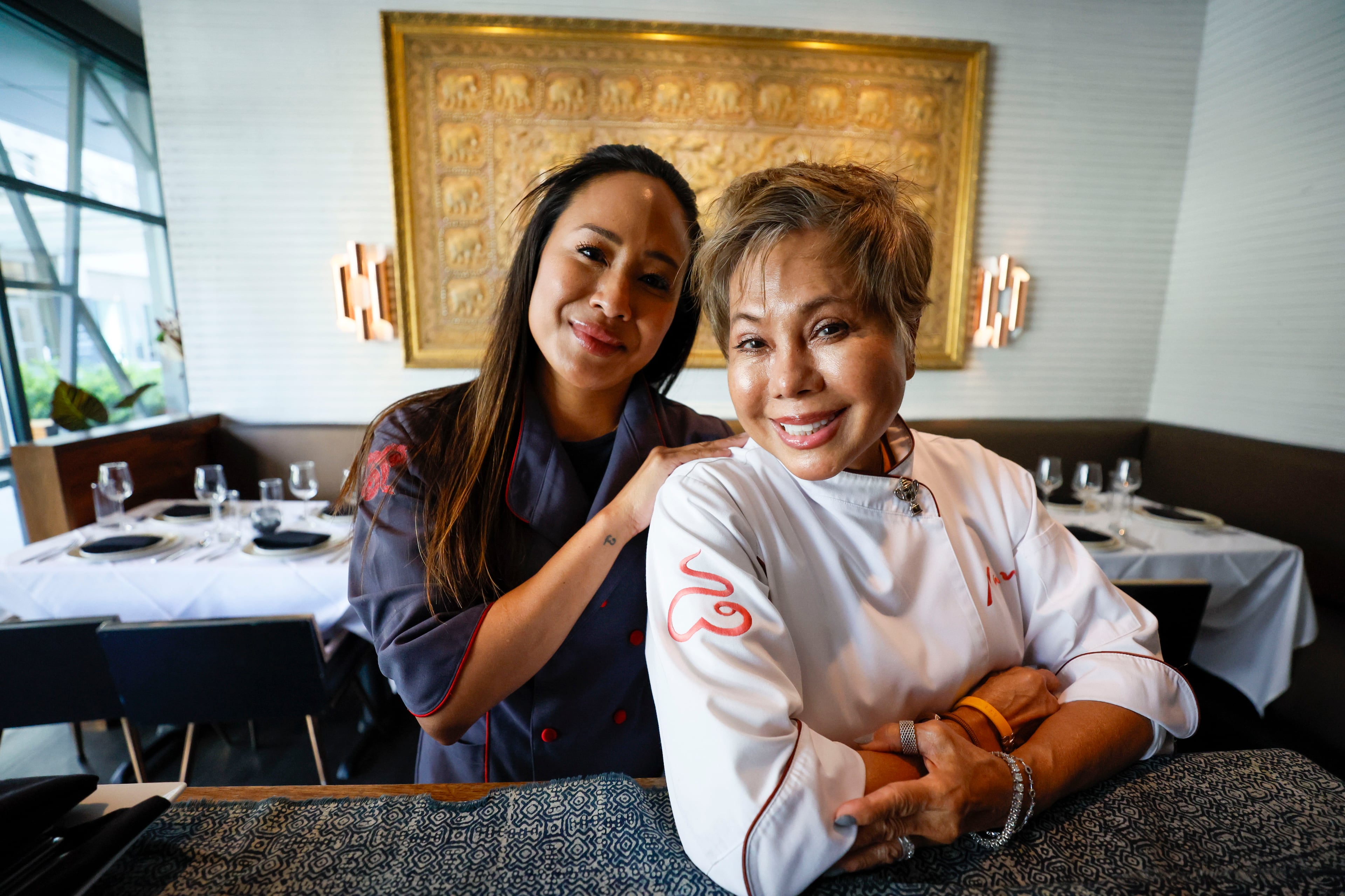 DeeDee Niyomkul and her mother, Nan Niyomkul, are shown at Nan Thai Buckhead in front of a tapestry that Nan brought from Thailand and displayed in the family's first restaurant in Manhattan almost 40 years ago. Nan shares her culinary expertise with DeeDee, who owns Tuk Tuk Thai Food Loft in Brookwood Hills and Nan Thai Buckhead. (Miguel Martinez/AJC)