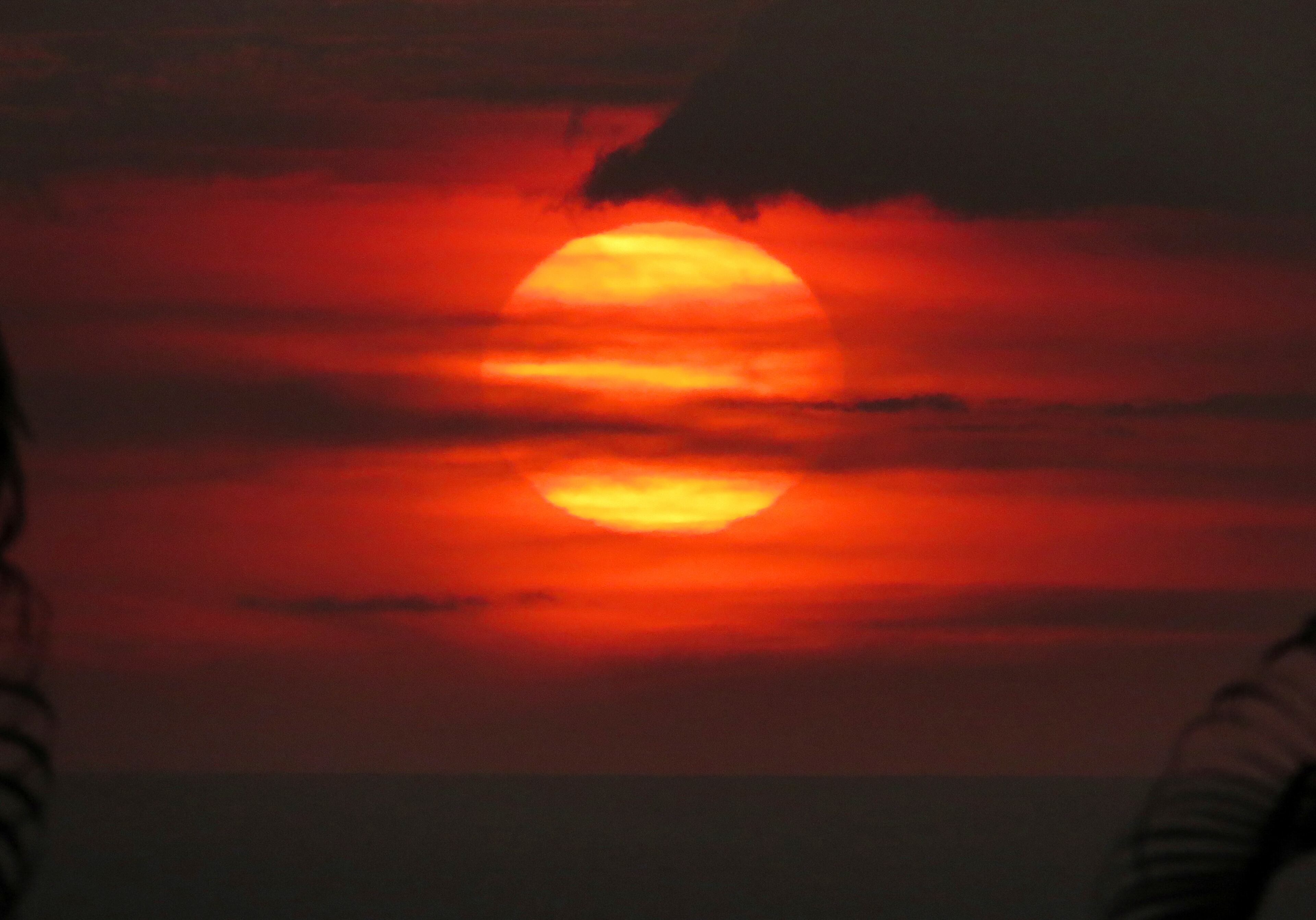 In this May 23, 2018, photo provided by Chris Stewart the sun sets through âvog,â or volcanic smog, in Kailua-Kona, Hawaii. Kilauea volcano on Hawaiiâs Big Island has had it all over the past three weeks: molten rock shooting toward the sky, lava oozing from the ground and ash clouds rising miles into the air. You can also add "vog" to the mix. Retired photojournalist Chris Stewart says thereâs one good thing about vog: It intensifies the colors of a sunset. But it depends on how thick the haze is. âSome days itâs thin enough you can see the sun passing through,â he said. âBut other days we just go inside because we canât see it at all.â (Chris Stewart via AP)