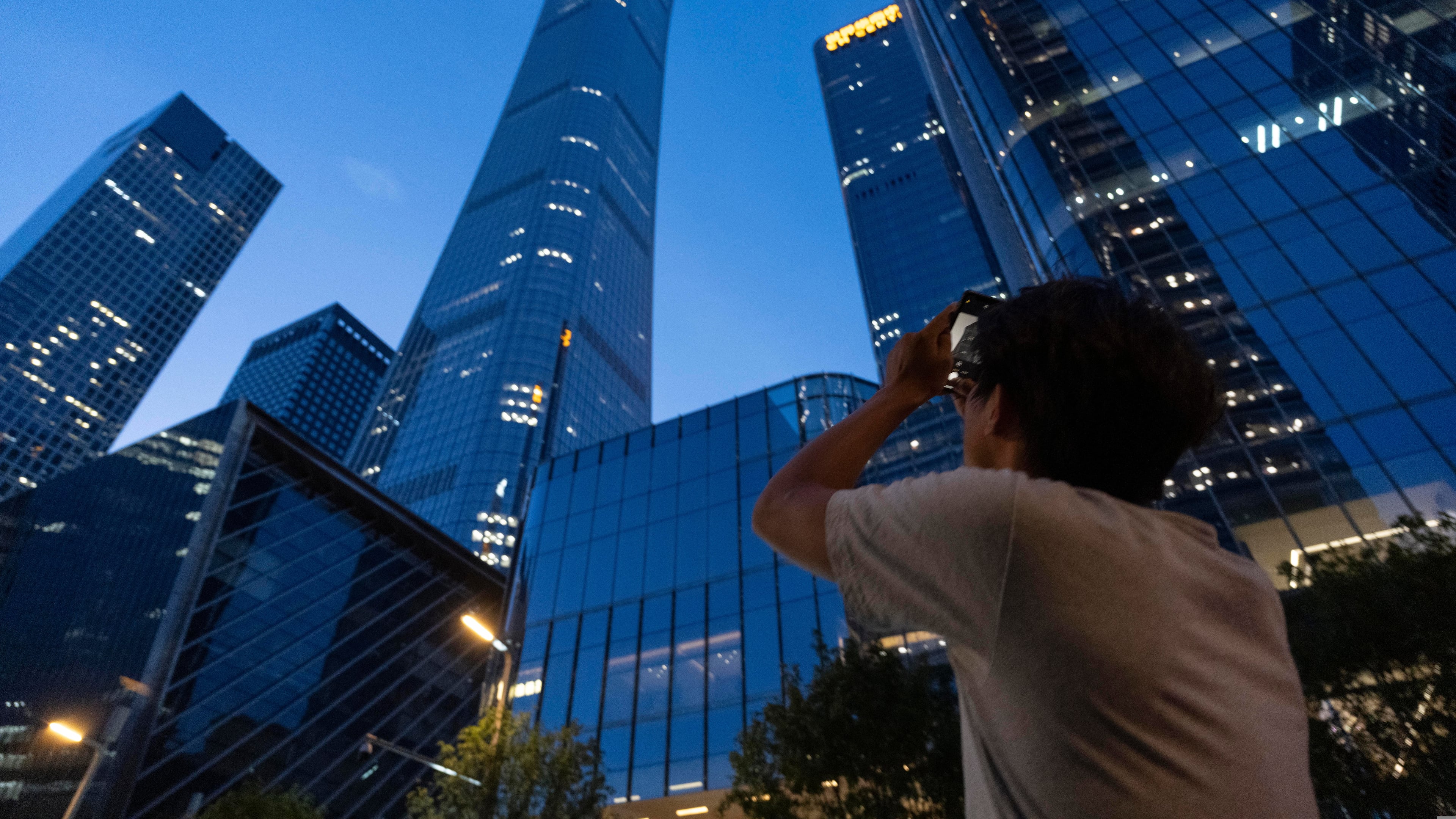 A passerby tries to take photo of the damage on the Citic Tower also known as Zun Tower in Beijing, China, Friday, June 26, 2026. (AP Photo/Han Guan Ng)