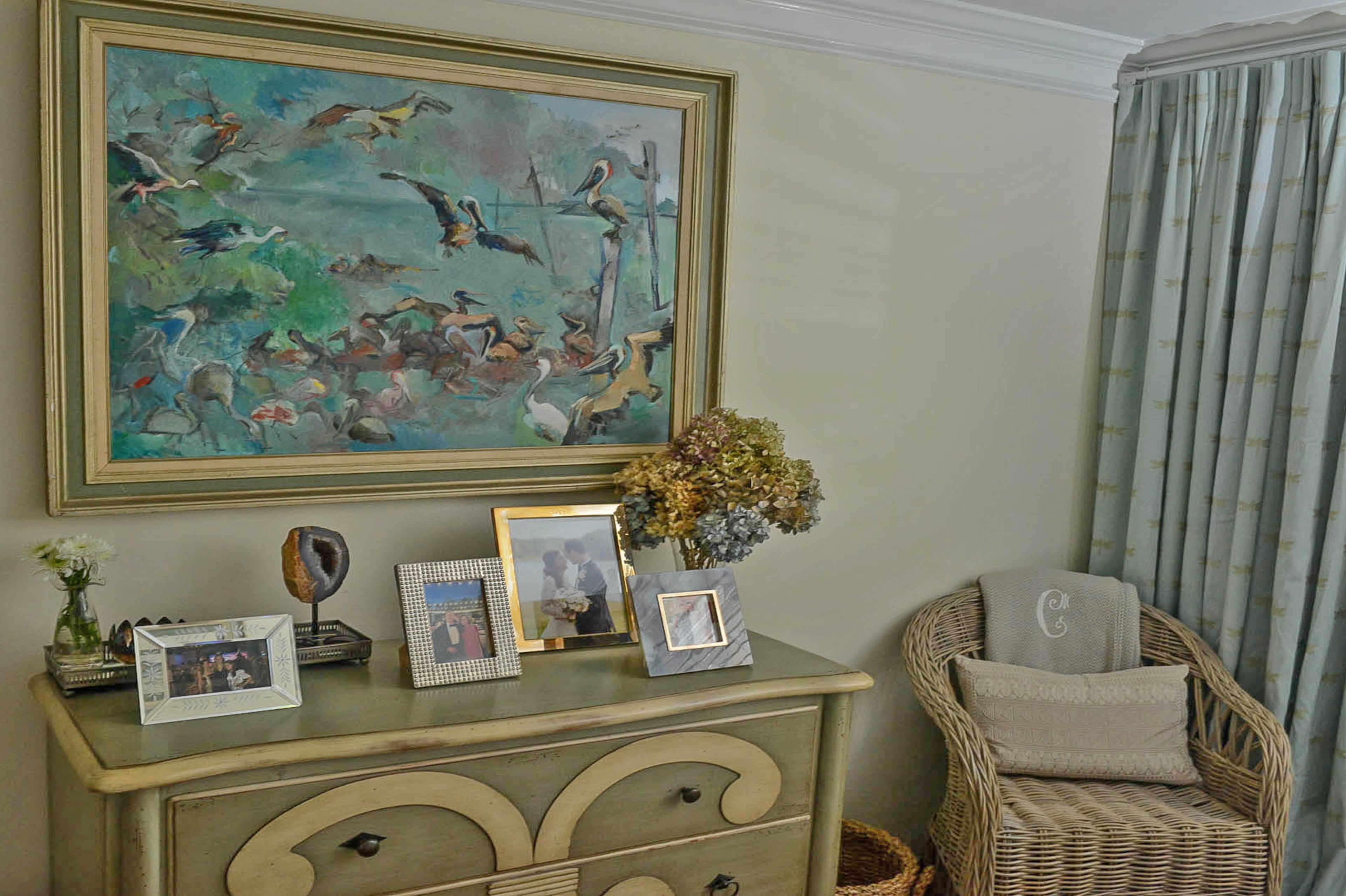 A painting by Gerry Bosch hangs above a carved and hand-painted chest of drawers borrowed from Elizabeth Cook's parents. The geode on the stand was found by Elizabeth's mother, and the agate frame is from Kendra Scott.