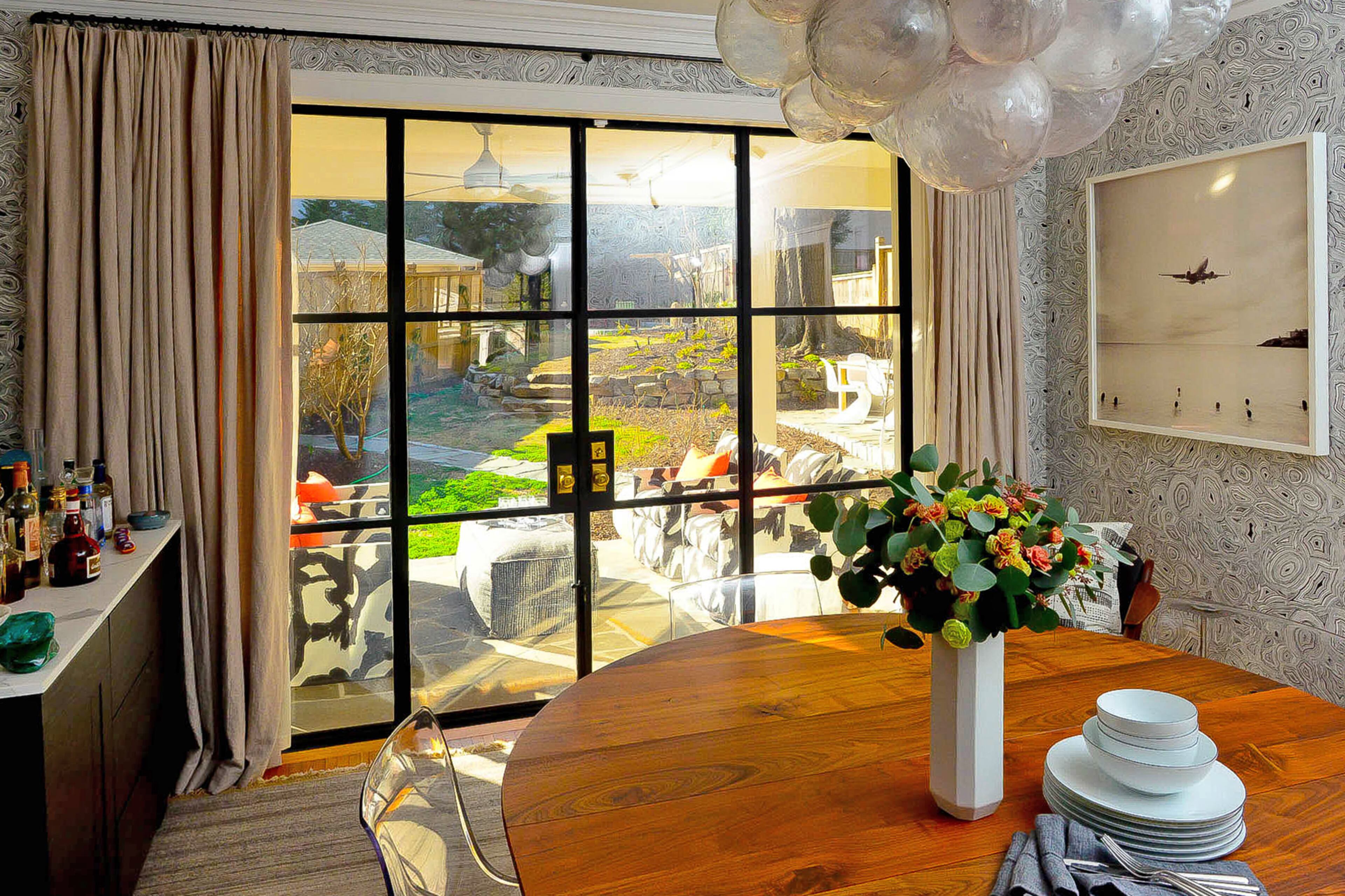 A modern update to the 1920s Craftsman is a wall of iron windows off the back, which makes indoor-outdoor living a breeze. The homeowner worked with contractor Gary Collins. The dining table crafted by Rough South Home is one of the custom pieces in the home, and the Malachite wallpaper is from the Fornasetti collection by Cole & Son. Oly's Muriel chandelier is a bubbly bonus.