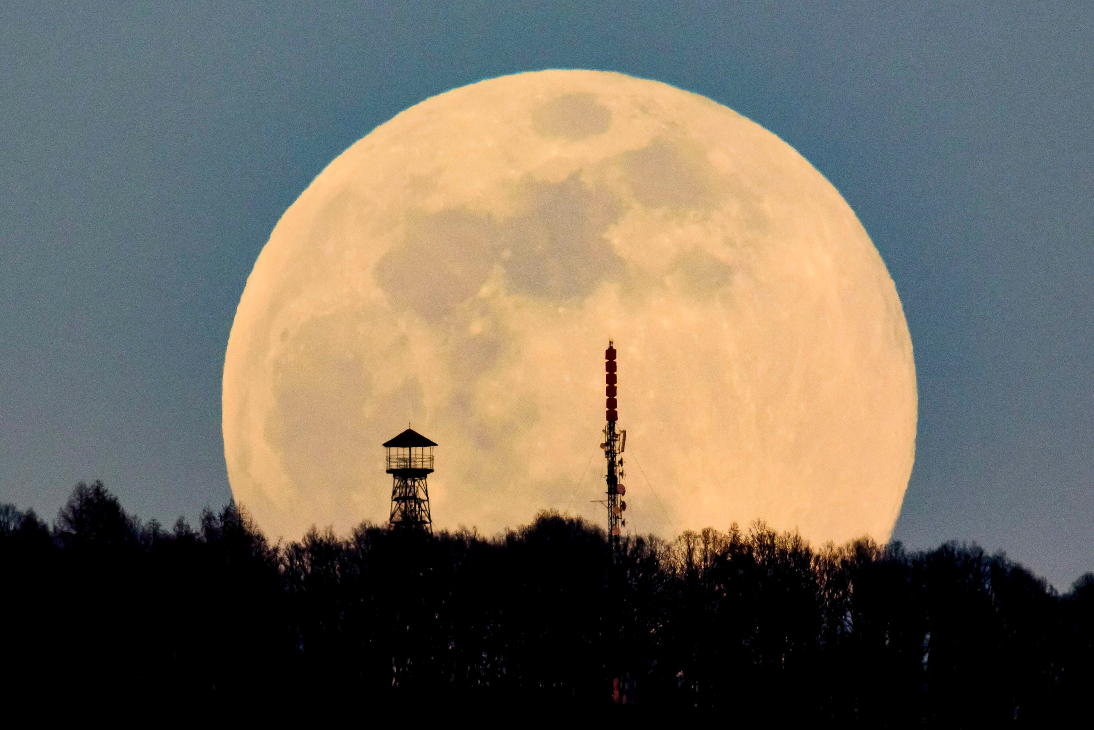 A lookout tower, left, and the broadcast tower of Antenna Hungaria at the top of Karancs mountain are backdropped by the rising moon as seen from the vicinity of Karancskeszi village, 128 kms northeast of Budapest, Hungary, Wednesday, March 20, 2019. (Peter Komka/MTI via AP)
