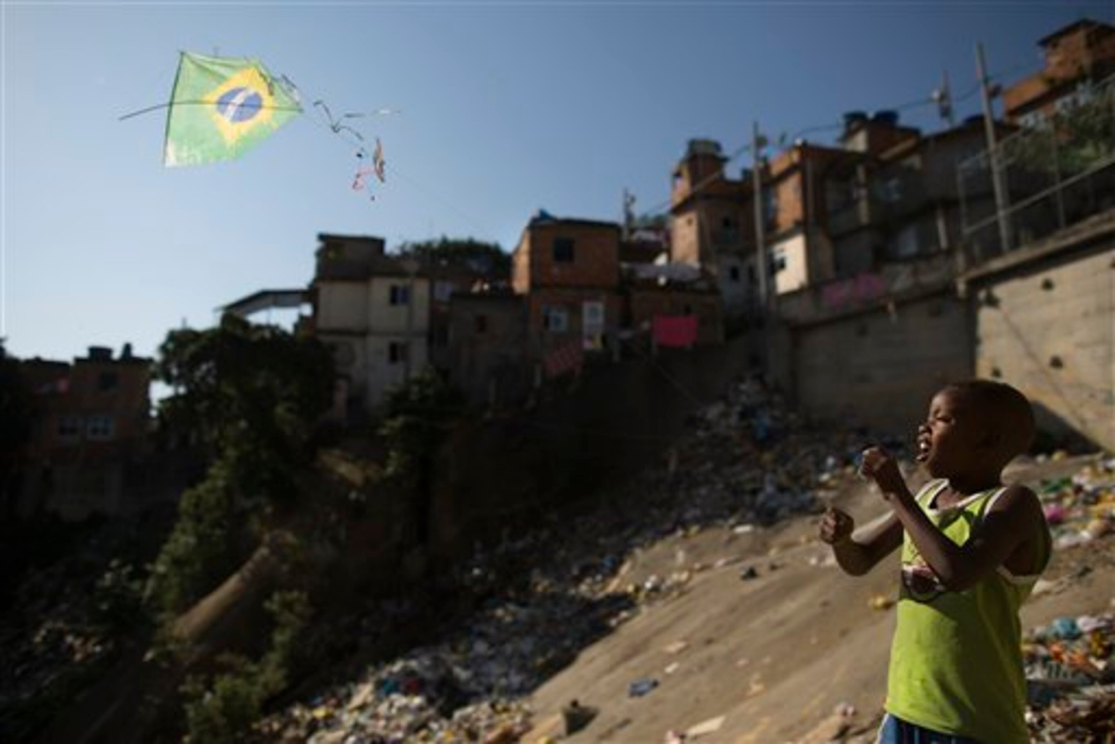 In this Monday, June 2, 2014 photo, a youth flies a kite in the likeness of Brazil's flag on a hillside in the Mangueira slum in Rio de Janeiro, Brazil. Brazil is hosting this year's World Cup soccer tournament that starts next week. (AP Photo/Leo Correa)