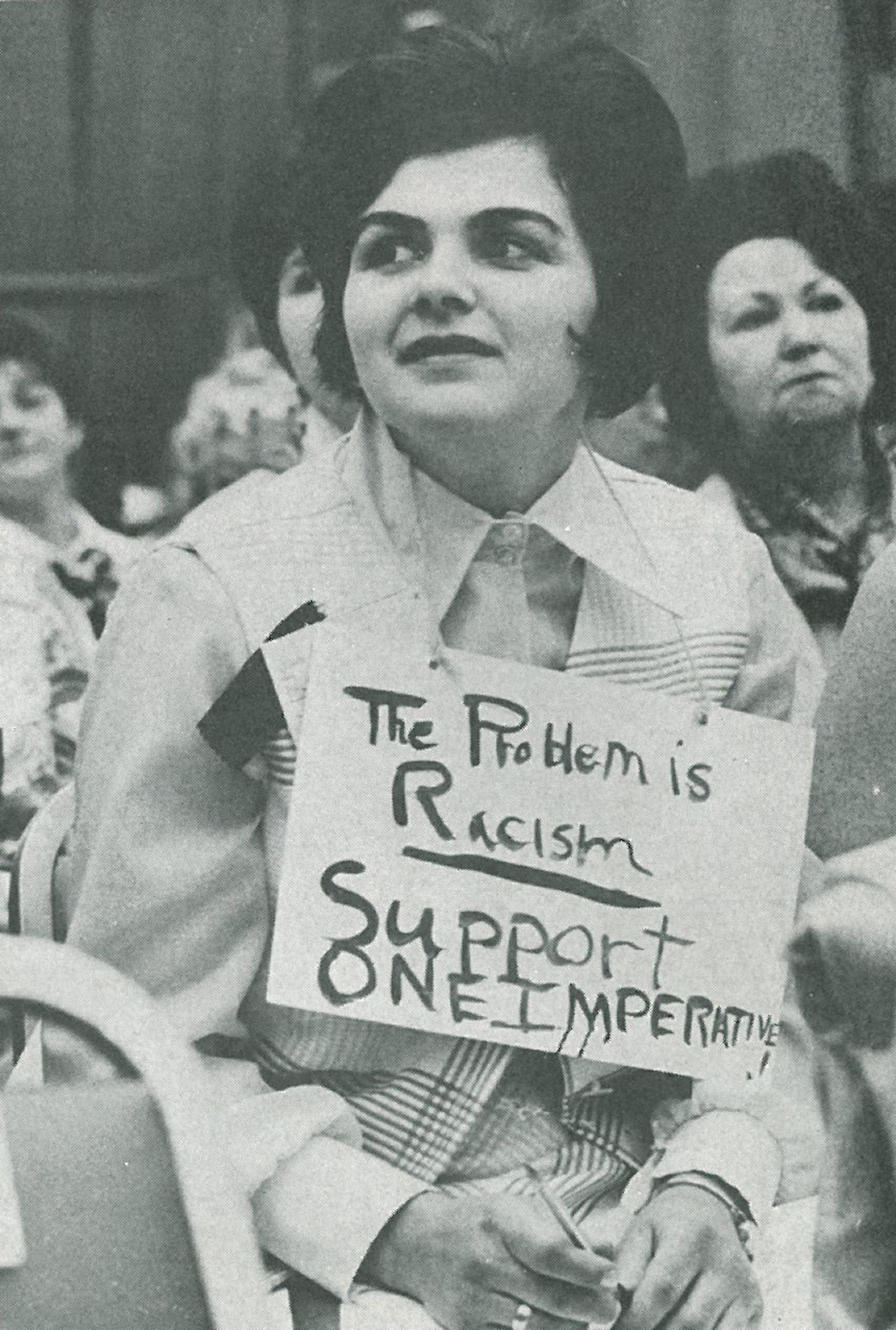A woman dons a sign saying "The problem is racism | Support One Imperative." (Courtesy of the YWCA)