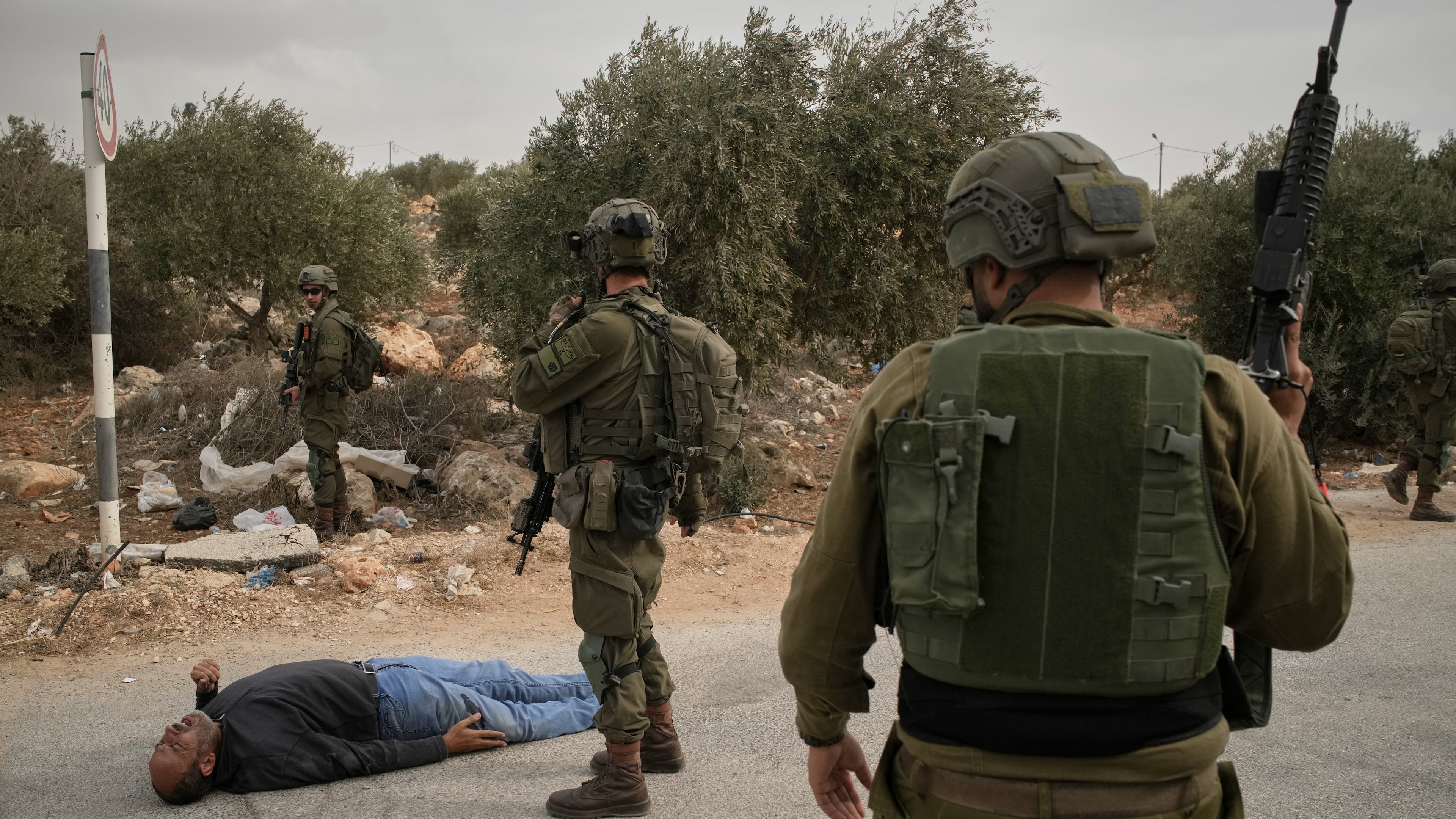 Israeli soldiers stand beside a wounded Palestinian man lying on a road after soldiers shot him following a settler attack on Palestinians harvesting olives in the occupied West Bank village of Abu Falah, Friday, Oct. 16, 2026. (AP Photo/Leo Correa)
