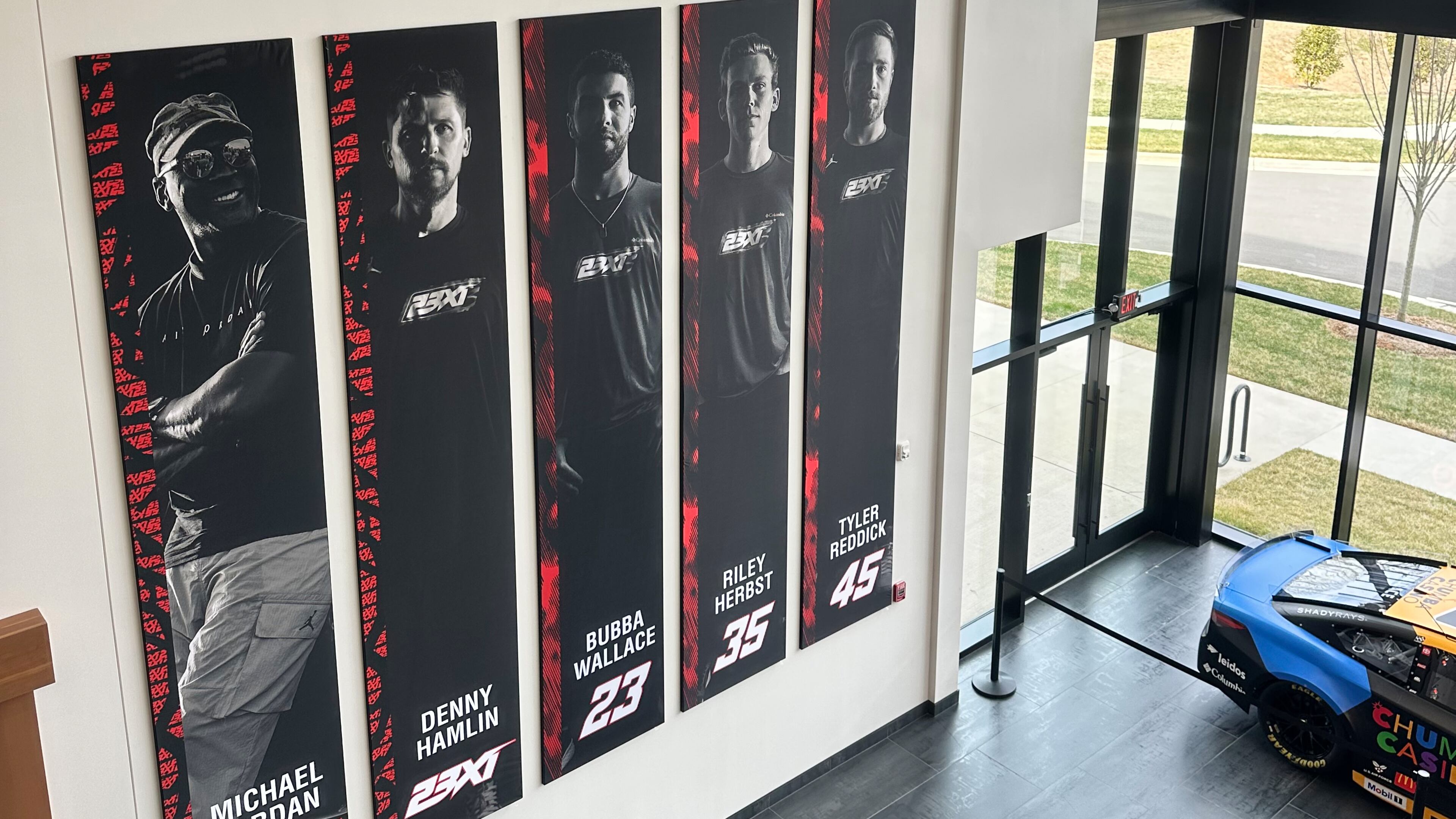 A banner, showing co-owners Michael Jordan and Denny Hamlin, as well as drivers Bubba Wallace, Corey Heim and Tyler Reddick, hangs in the lobby at Airspeed, the headquarters of 23XI Racing, Tuesday, Feb. 24, 2026 in Huntersville, N.C. (AP Photo/Jenna Fryer)