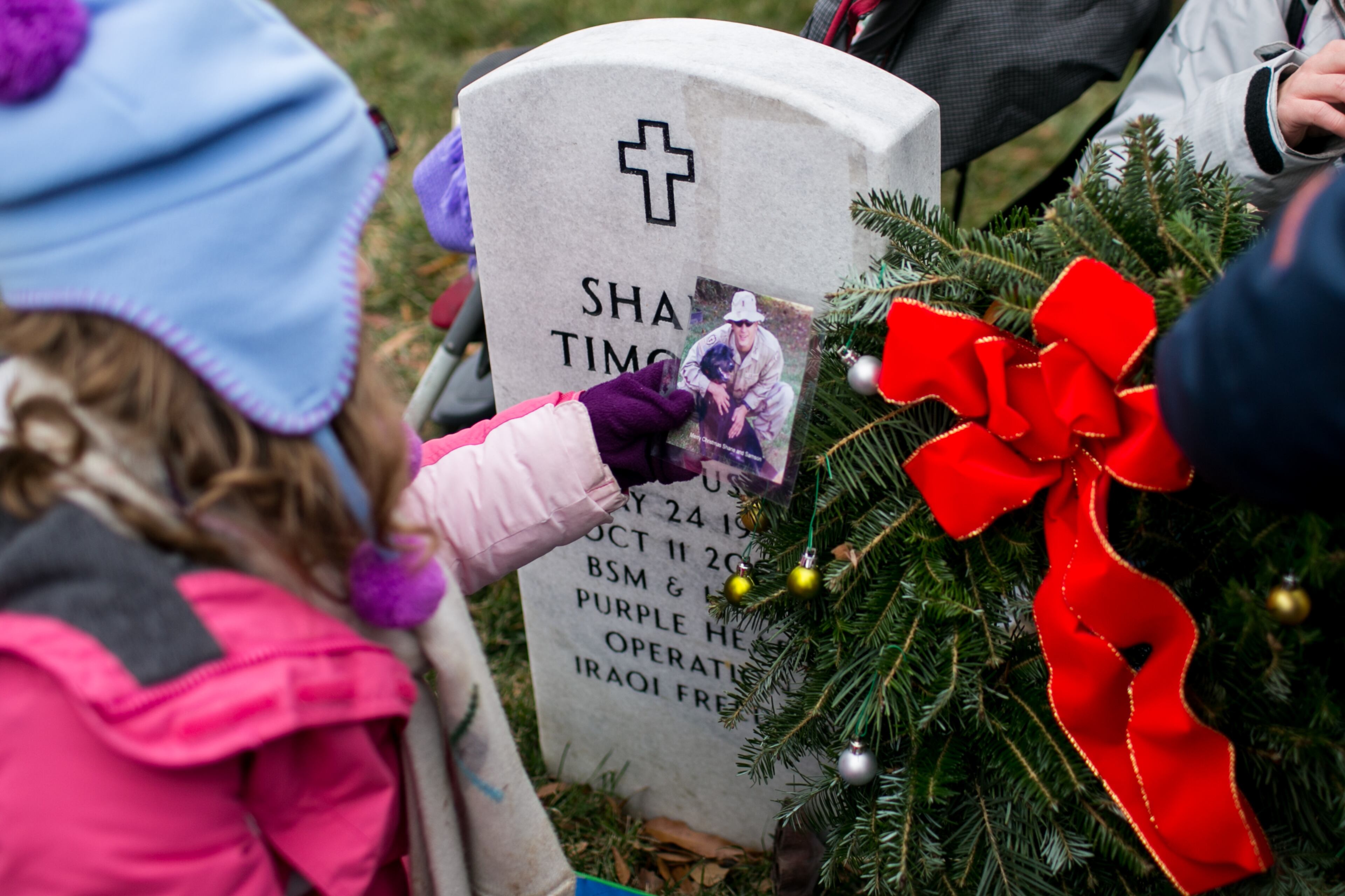 ARLINGTON, VA - DECEMBER 14: Family and friends gather at the headstone of Army Capt. Shane Timothy Adcock in Section 60 of Arlington National Cemetery, December 14, 2013 in Arlington, Virginia. Adcock died on October 11, 2006, in Hawijah, Iraq, from injuries suffered from enemy grenade fire. Volunteers and families of the fallen placed thousands of remembrance wreaths on headstones throughout the cemetery on National Wreaths Across America Day. (Photo by Drew Angerer/Getty Images)