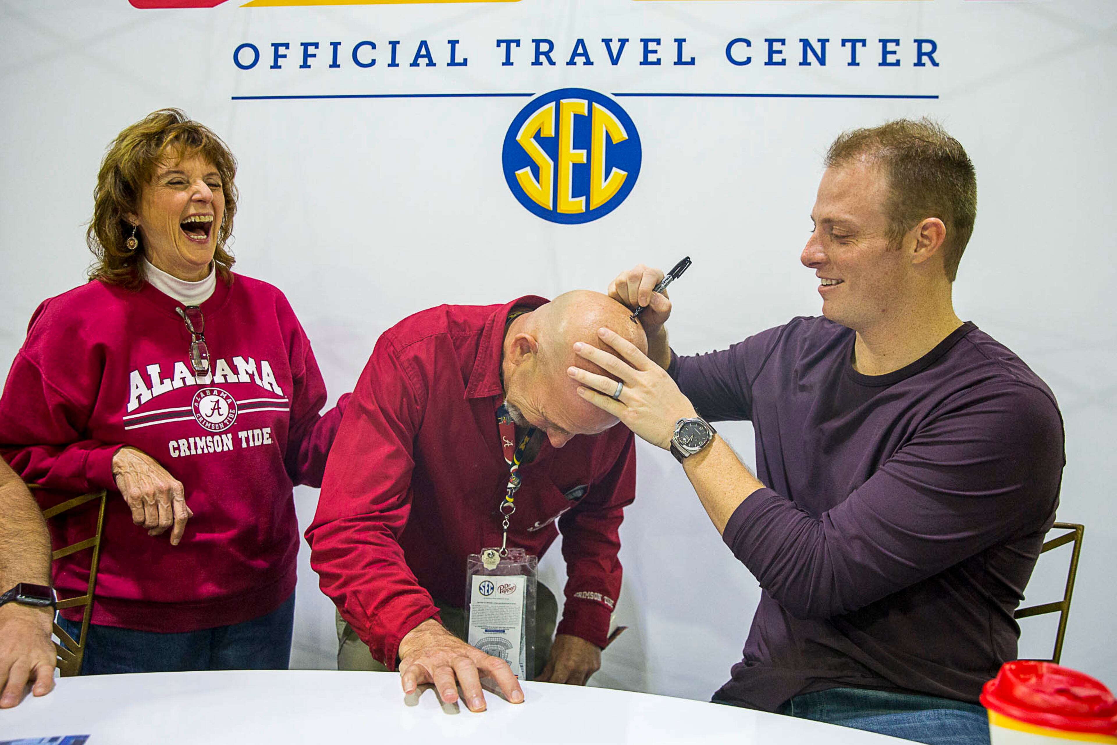 12/01/2018 -- Atlanta, Georgia -- Donna Peters (left) laughs as her friend William "Billy" Brink (center) gets his head signed by former University of Alabama quarterback Greg McElroy Jr. (right) at the Dr. Pepper SEC FanFare experience at the Georgia World Congress Center in Atlanta, Saturday, December 1, 2018. McElroy scribbled Roll Tide along with his signature a top Brink's hairless head. (ALYSSA POINTER/ALYSSA.POINTER@AJC.COM)