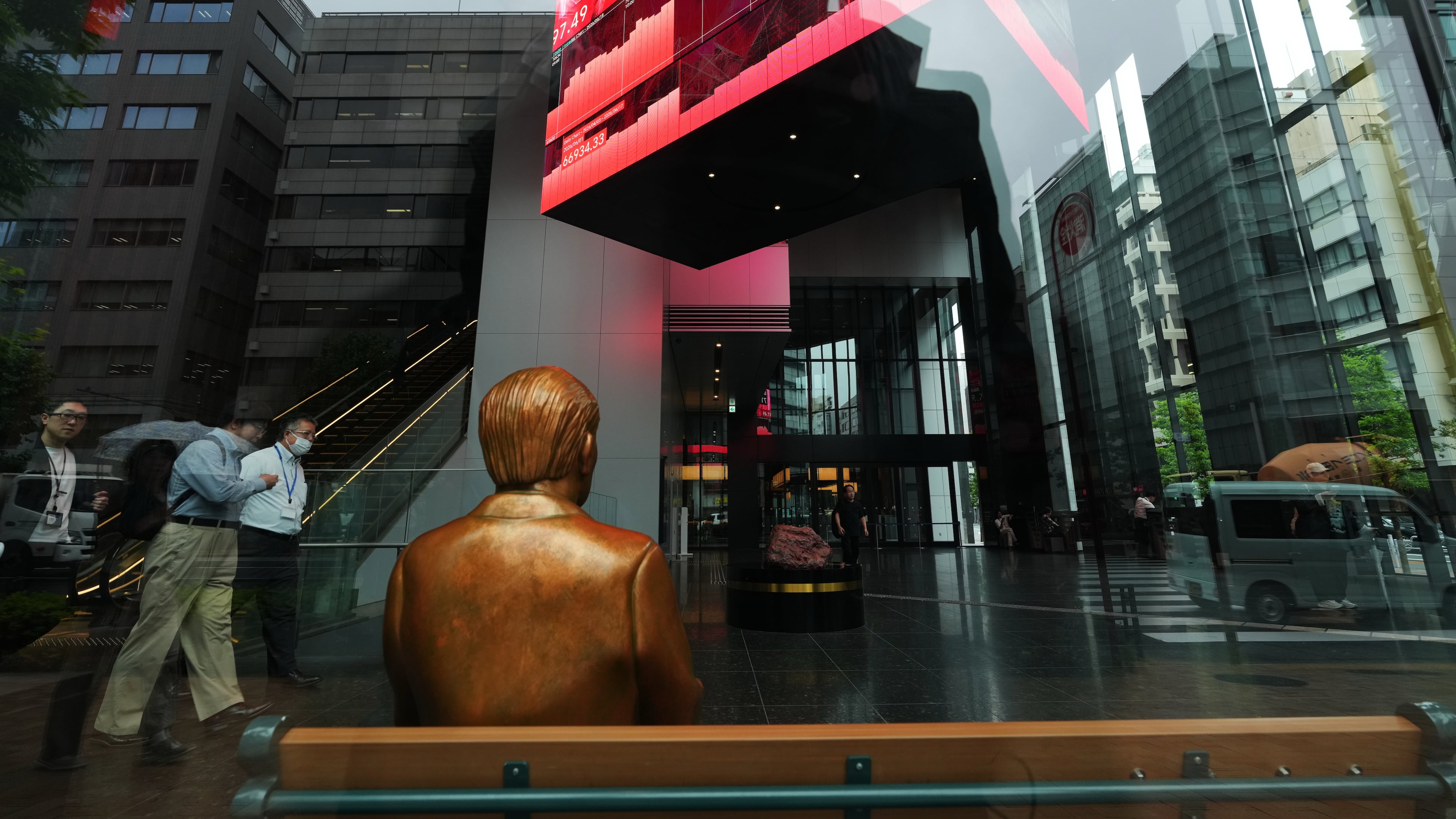 A statue is placed on a bench near monitors showing Japan's Nikkei 225 index, hanging in a business building in Tokyo, Thursday, June 18, 2026. (AP Photo/Hiro Komae)