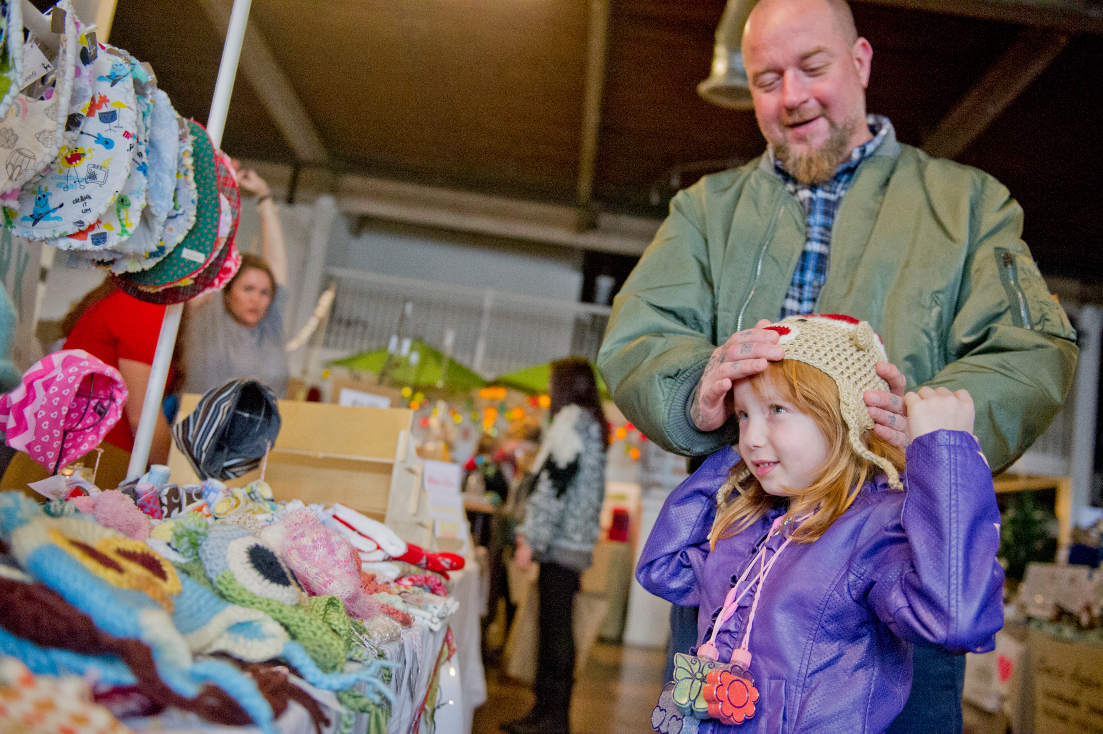 Charlee Thrice (right) tries on a hand made hat with help from her father Eric at the LylahG booth during the Indie Craft Experience at Ambient Plus Studio in Atlanta on Nov. 23, 2013.