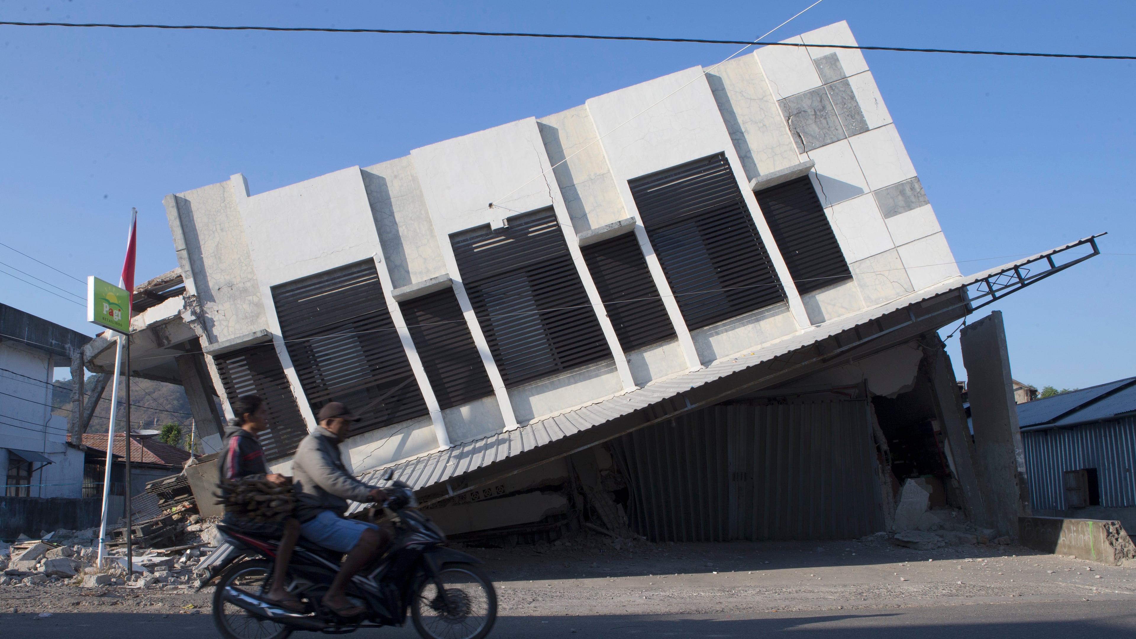Motorists ride past a building that collapsed during an earthquake in Reo, East Nusa Tenggara province, Indonesia, Monday, Aug. 17, 2026. (AP Photo/Firdia Lisnawati)