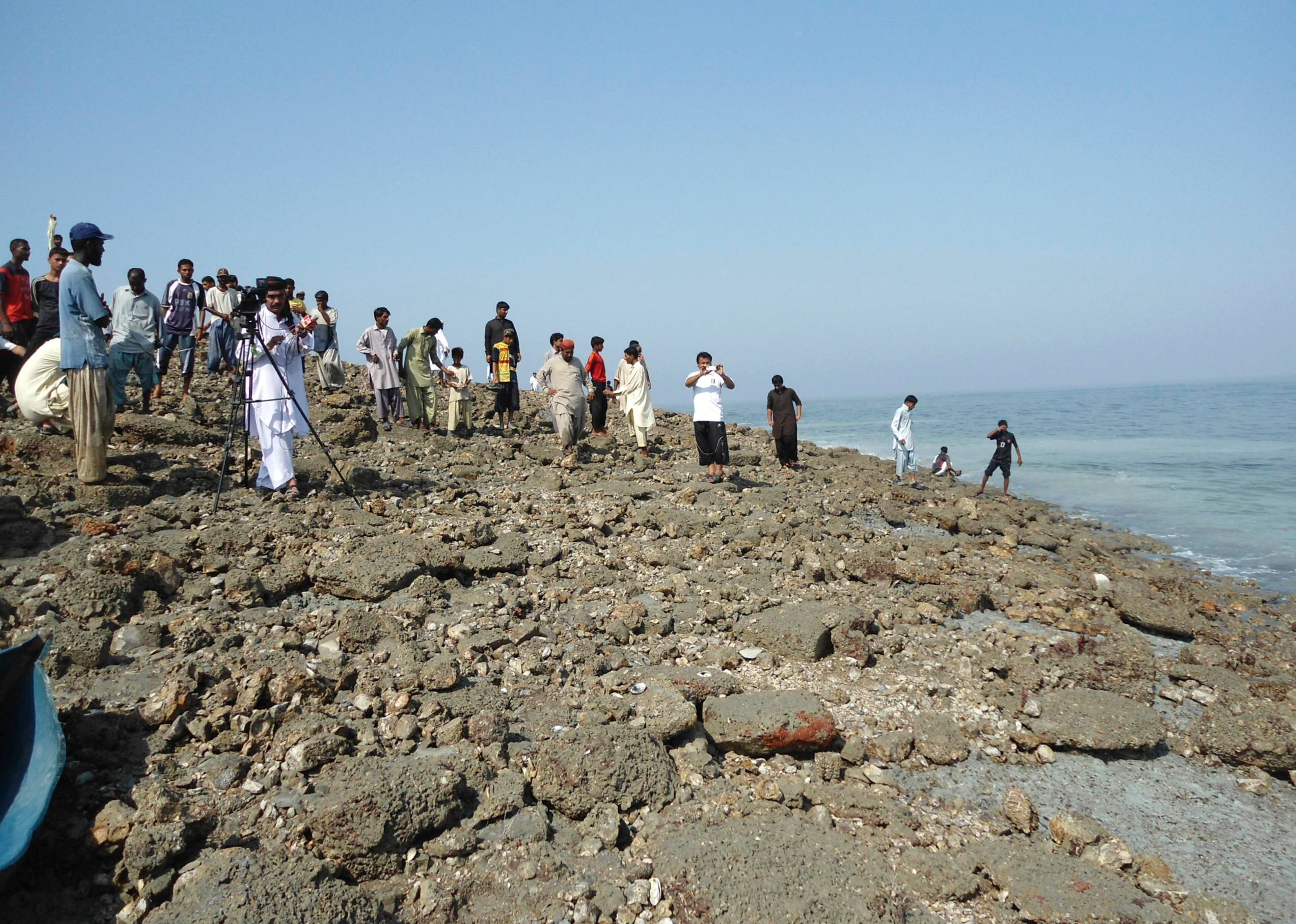 Members of the media and people walk on an island that rose from the sea following an earthquake off Pakistan's Gwadar coastline in the Arabian Sea September 25, 2013.