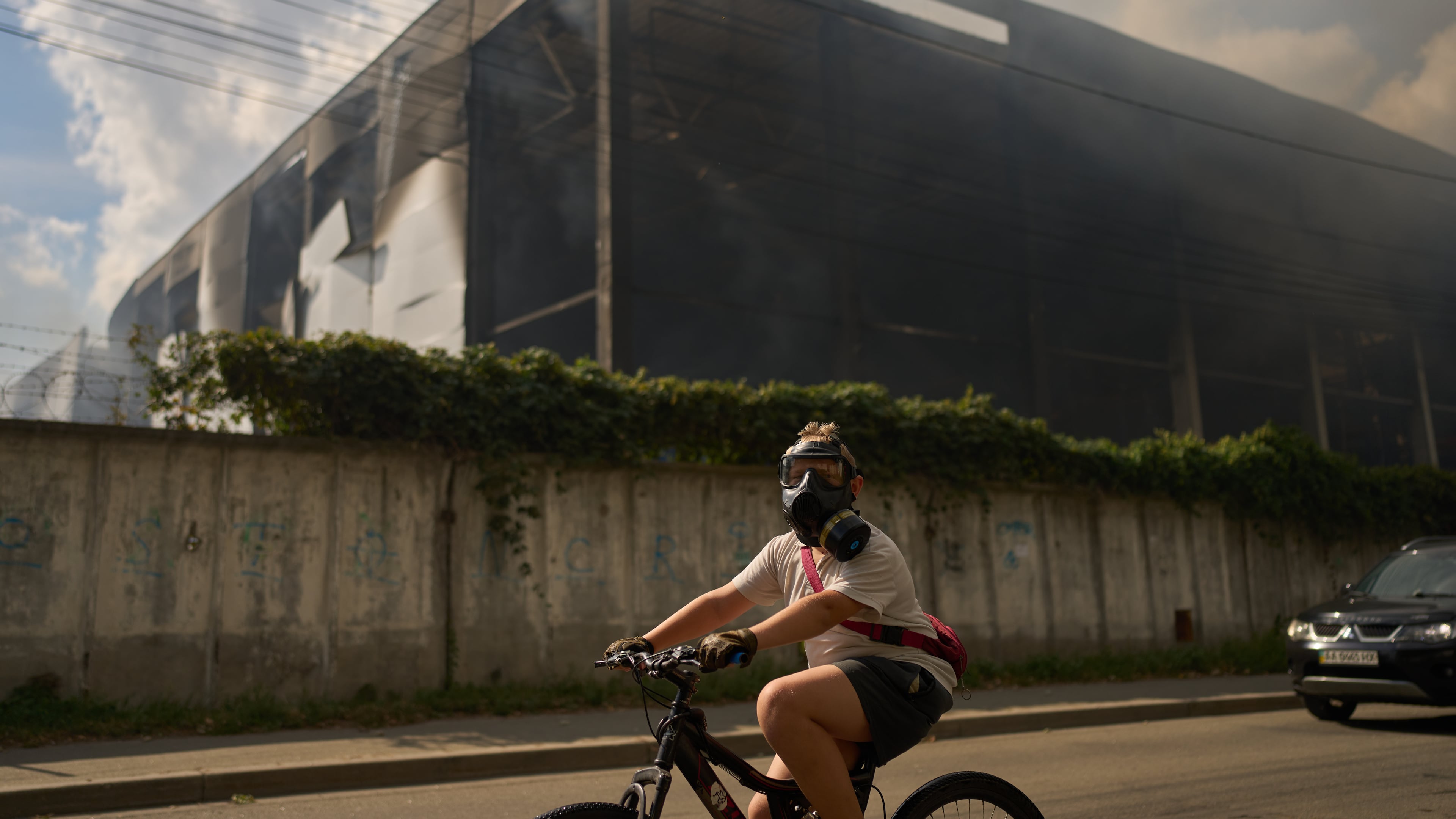 A local resident wears a gas mask as he rides a bicycle past a partially destroyed warehouse after a Russian drone attack in Brovary on the outskirts of Kyiv, Ukraine, Friday, Sept. 4, 2026. (AP Photo/Francisco Seco)