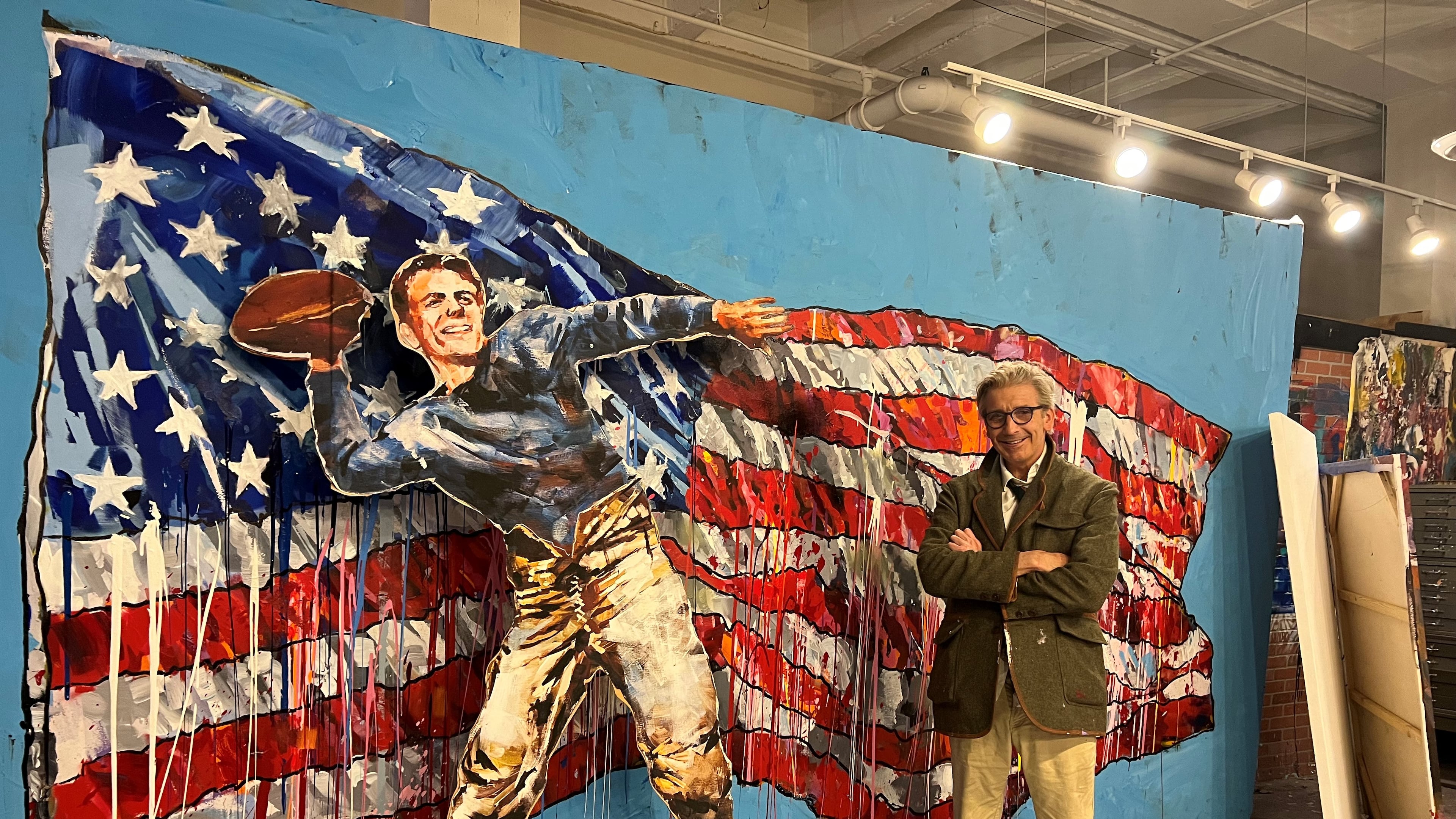Artist Steve Penley stands in his Atlanta studio alongside recent paintings of Ronald Reagan and the American flag.