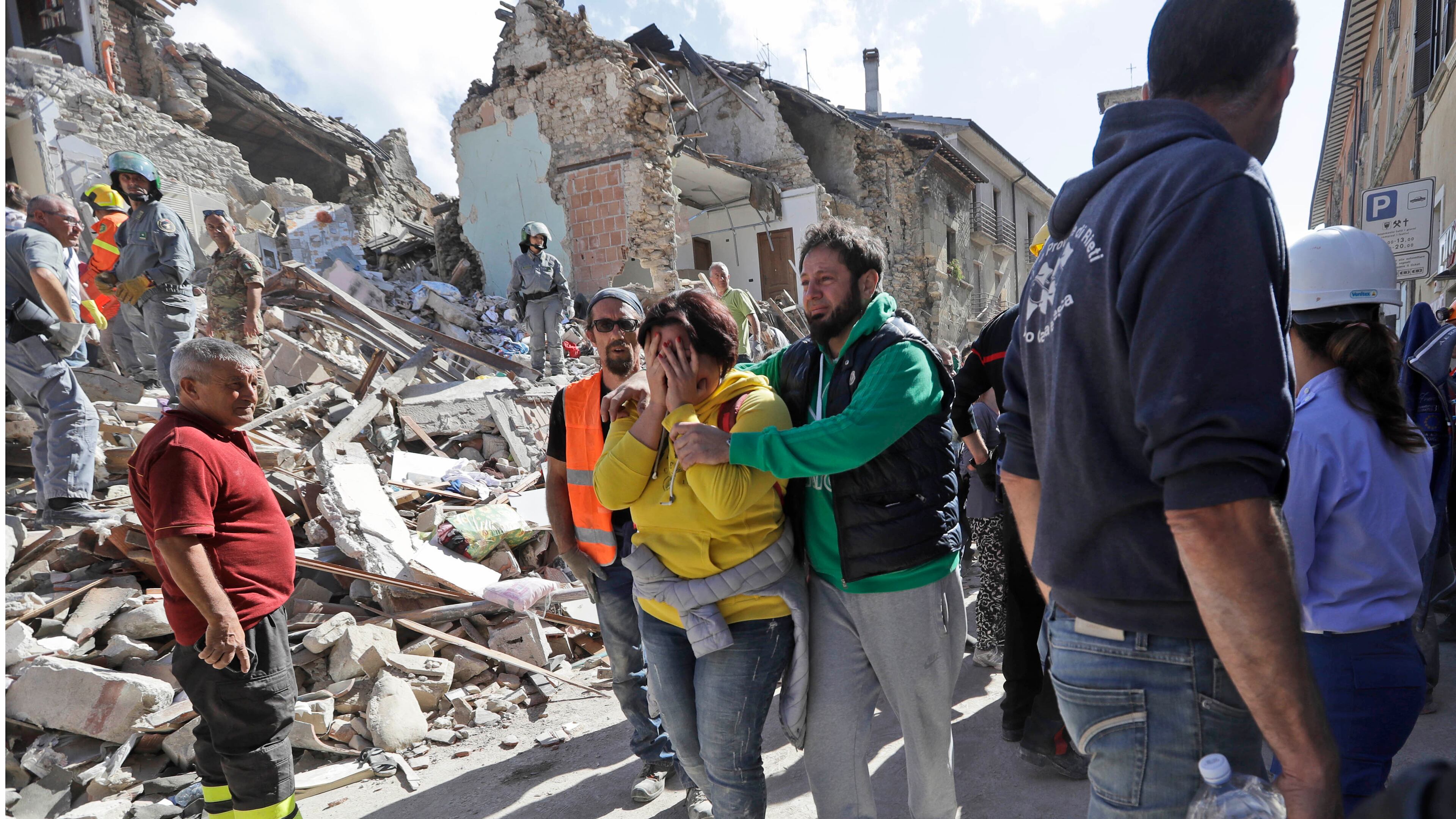 A woman is comforted as she walks through rubble after an earthquake, in Amatrice, central Italy, Wednesday, Aug. 24, 2016. A devastating earthquake rocked central Italy early Wednesday, collapsing homes on top of residents as they slept. At least 23 people were reported dead in three hard-hit towns where rescue crews raced to dig survivors out of the rubble, but the toll was expected to rise as crews reached homes in more remote hamlets. (AP Photo/Alessandra Tarantino)