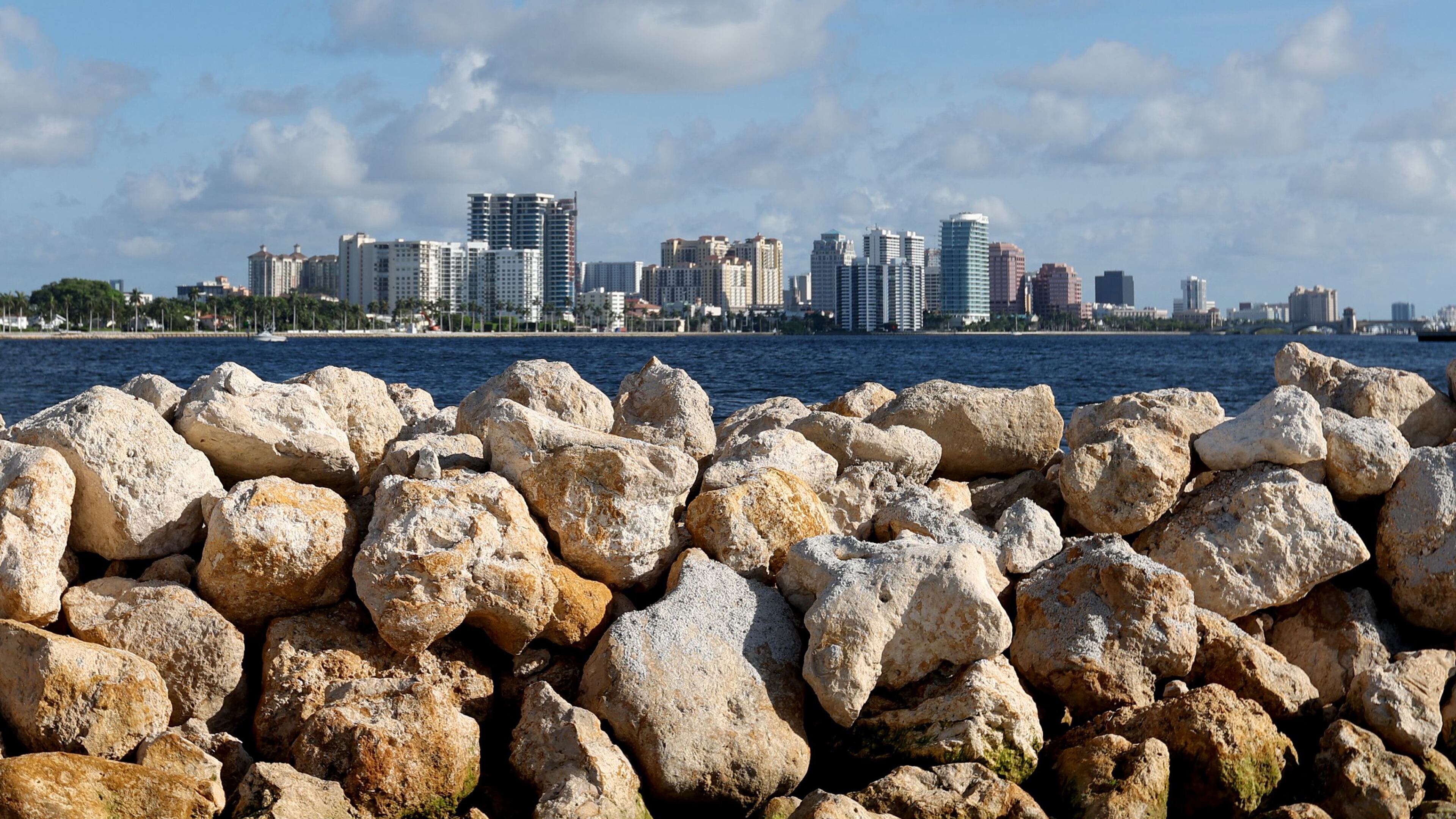 Limestone boulders meant to break up wave energy are stacked on a manmade island, part of the Palm Beach Resilient Island Project in the Tarpon Cove area near Lake Worth on July 1, 2022. Downtown West Palm Beach can be seen in the distance. The limestone will house oyster beds that naturally filter the water and abate nutrient pollution. (Amy Beth Bennett/South Florida Sun Sentinel/TNS)